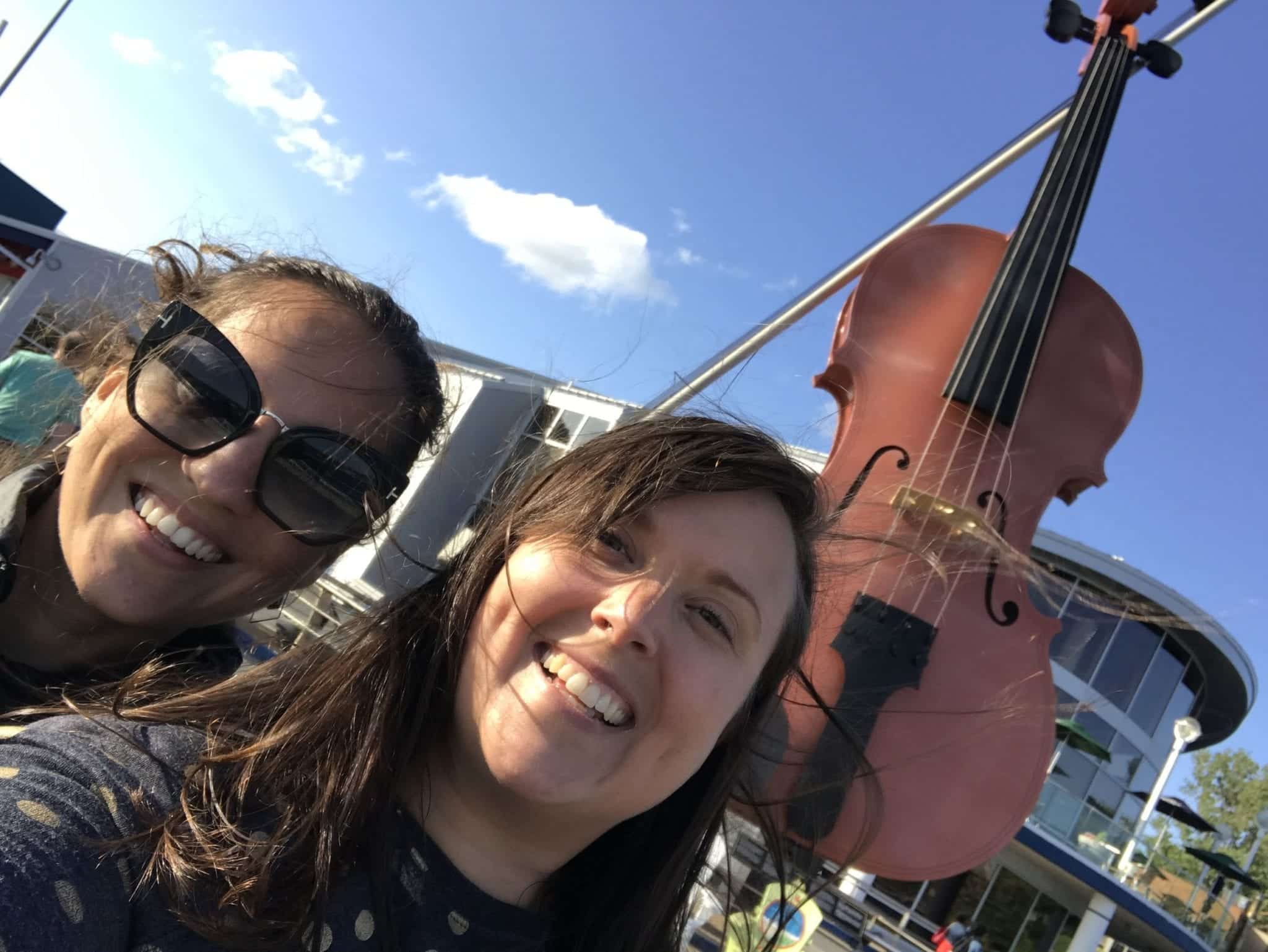 Kate and Cailin pose for a selfie in front of the giant fiddle, standing up in Sydney, Nova Scotia.