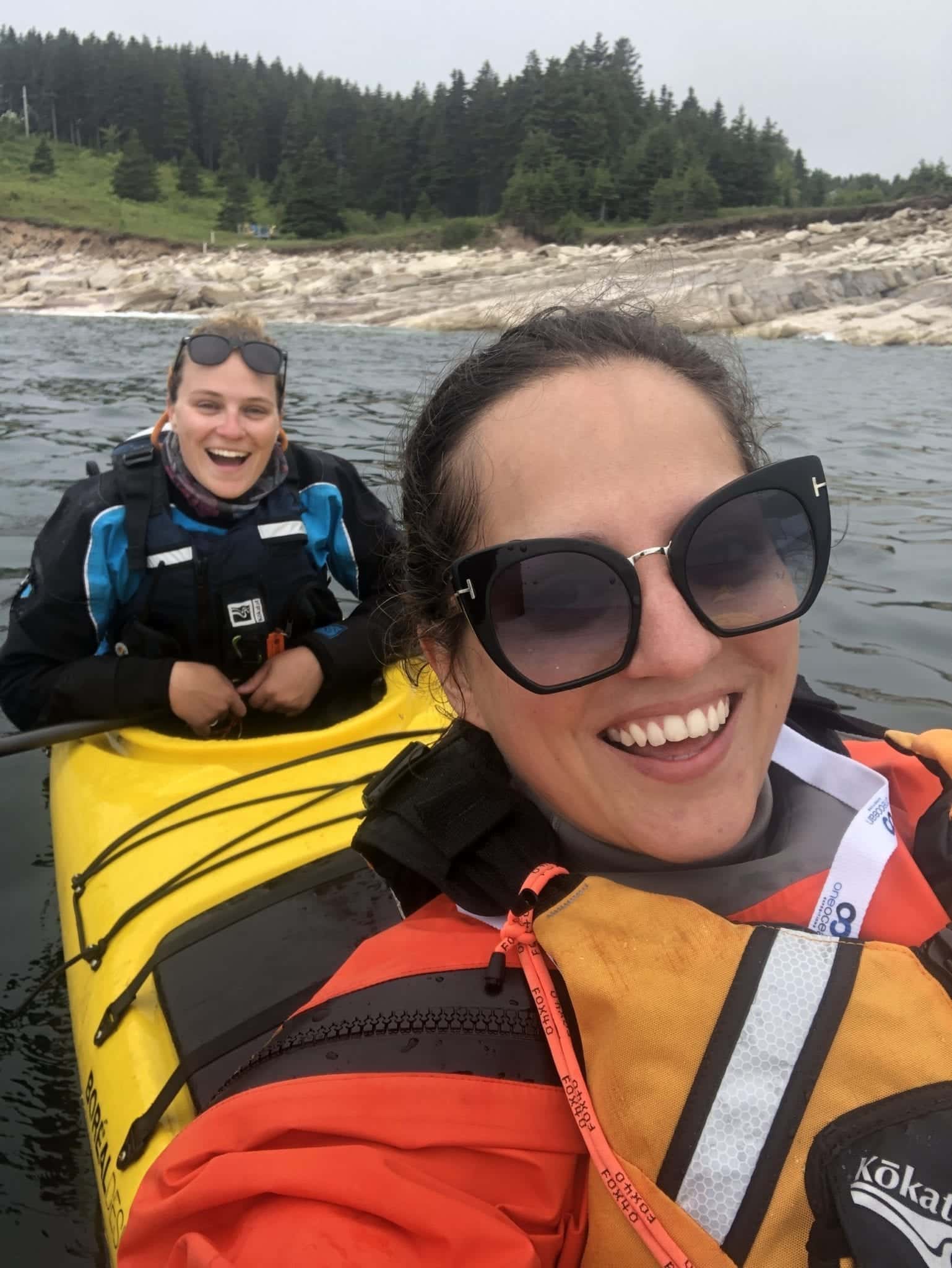 Kate takes a selfie from the front of a kayak as her friend Haley smiles from the back of the kayak.