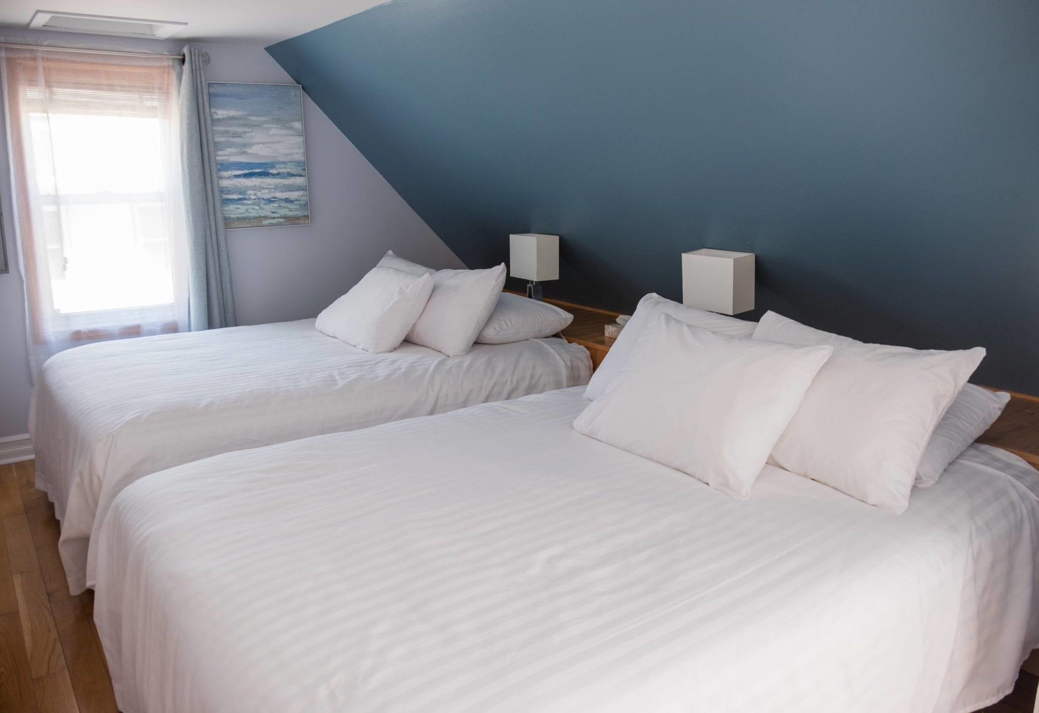 Two queen beds in white bedding with lots of pillows in Silver Linings Inn, Cheticamp, Nova Scotia.