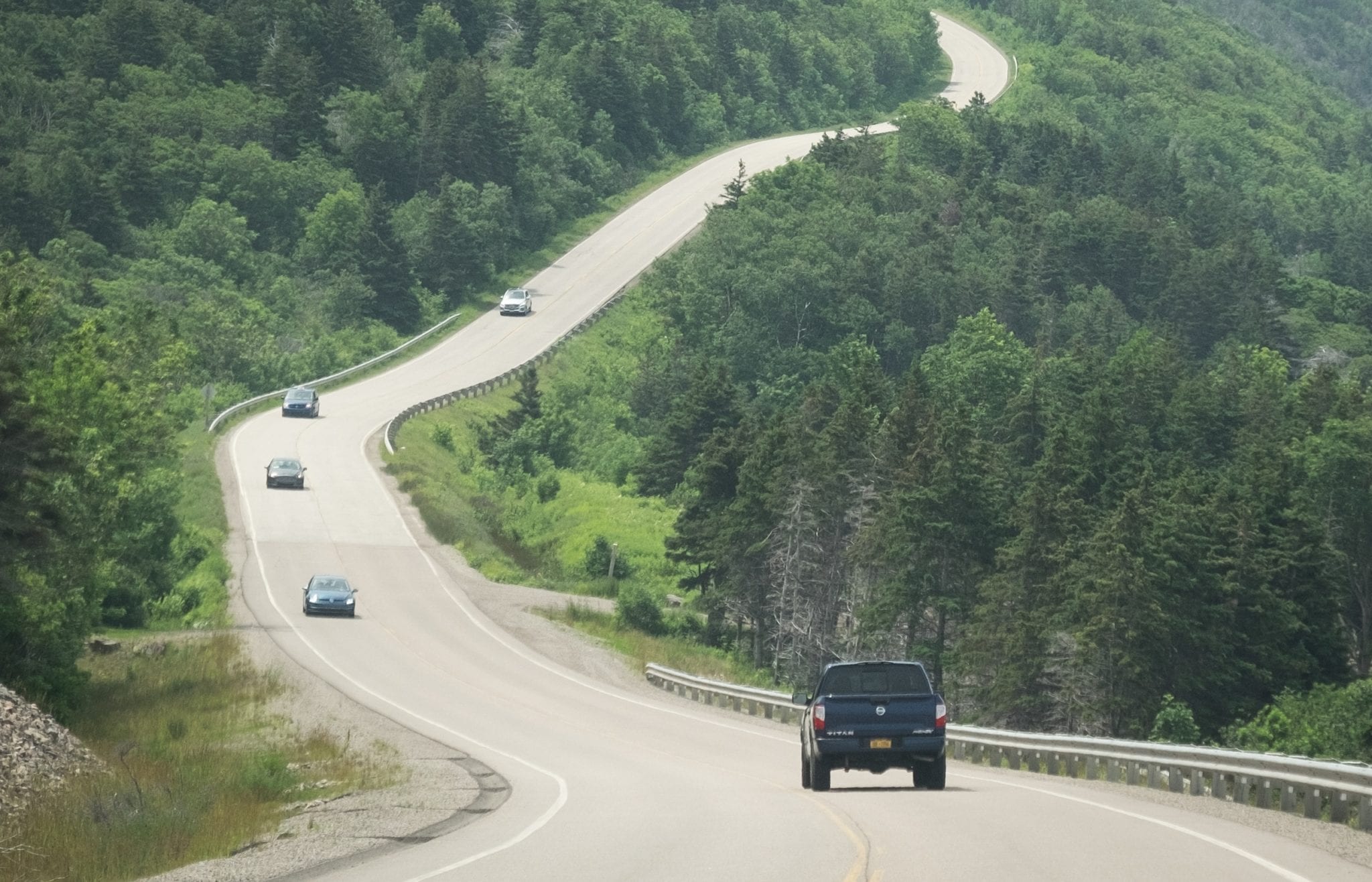 Cars driving along a curvy road on tree-covered mountains.