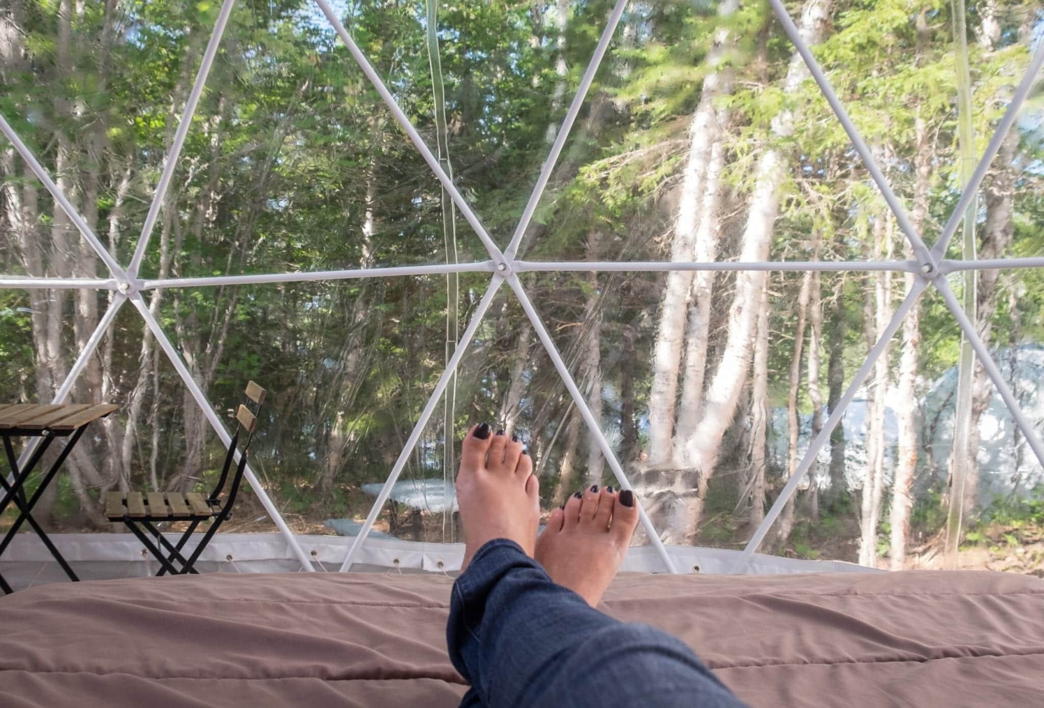 Kate's feet leaning off a bed in the Blue Bayou Geodesic Domes with the windows behind her feet and trees behind them.