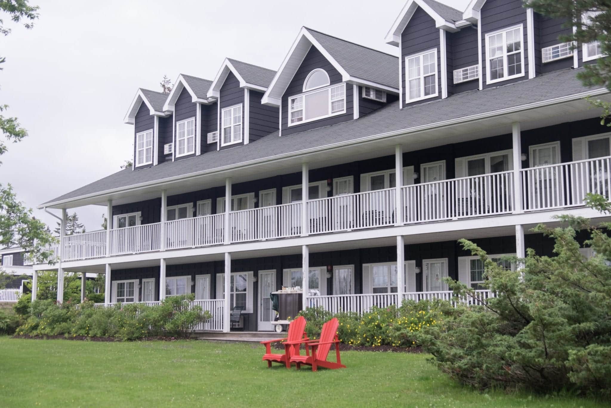 A navy blue house with white trim, porches in front, and two red chairs sitting on the ground in front of the house.