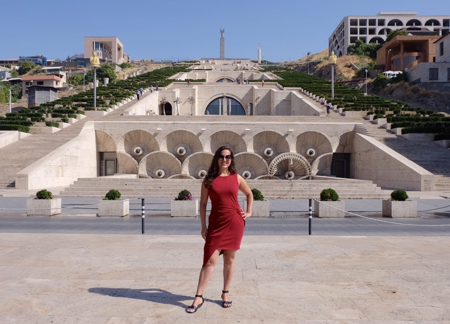 Kate wears a red dress and stands in the Cascade of Lebanon, a pyramid-shaped structure with staircases on each side.