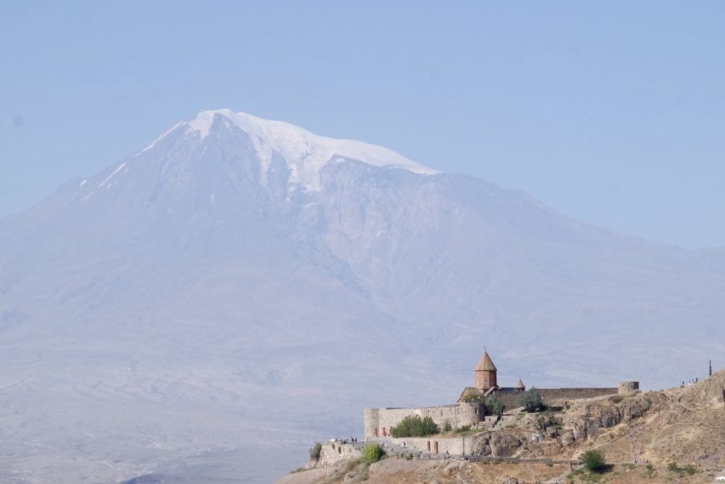 In the bottom right corner, Noravank monastery; in the rest of the background, a hazy blue view of Mount Ararat.
