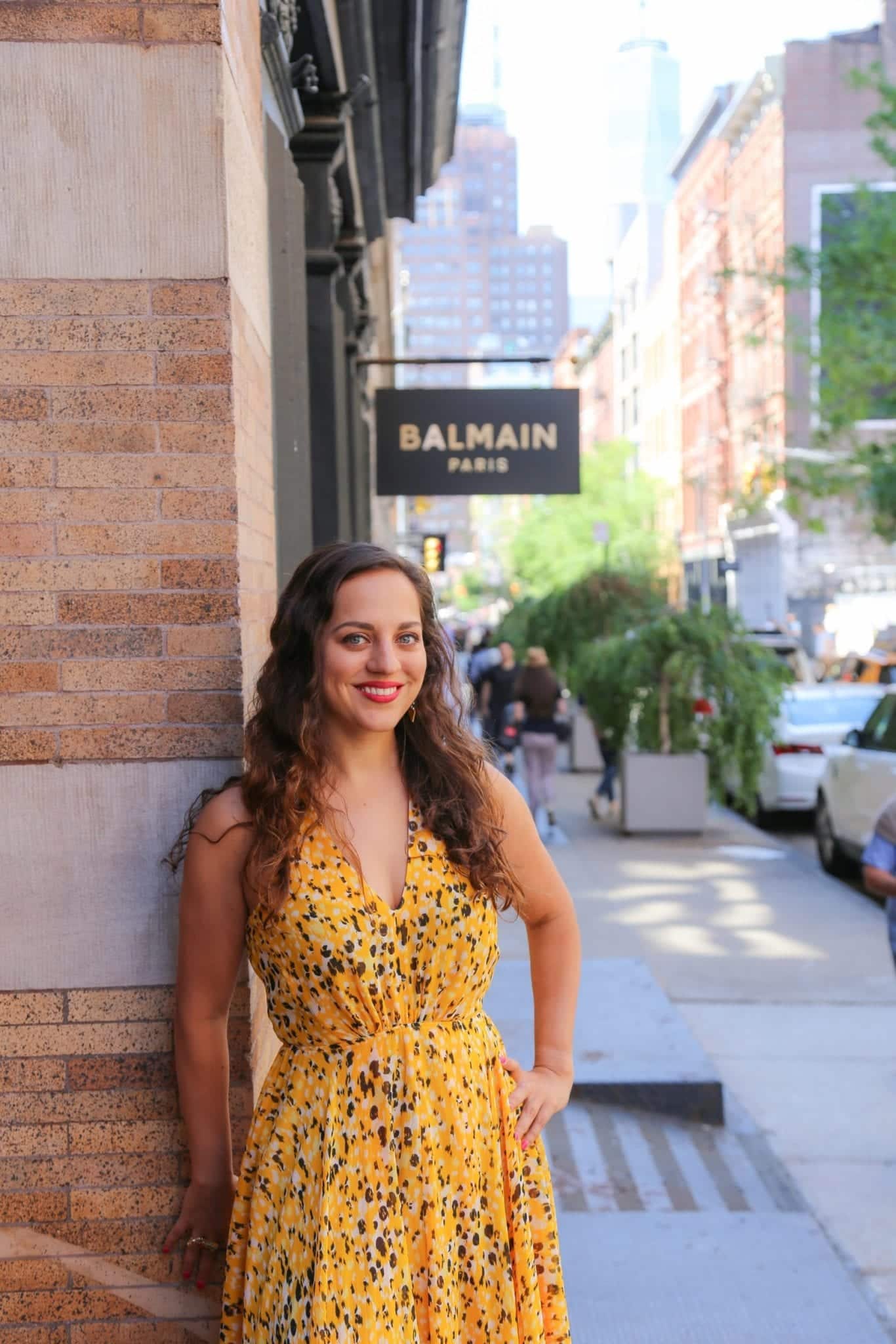 Kate in a yellow dress beneath the Balmain sign in SoHo, NYC