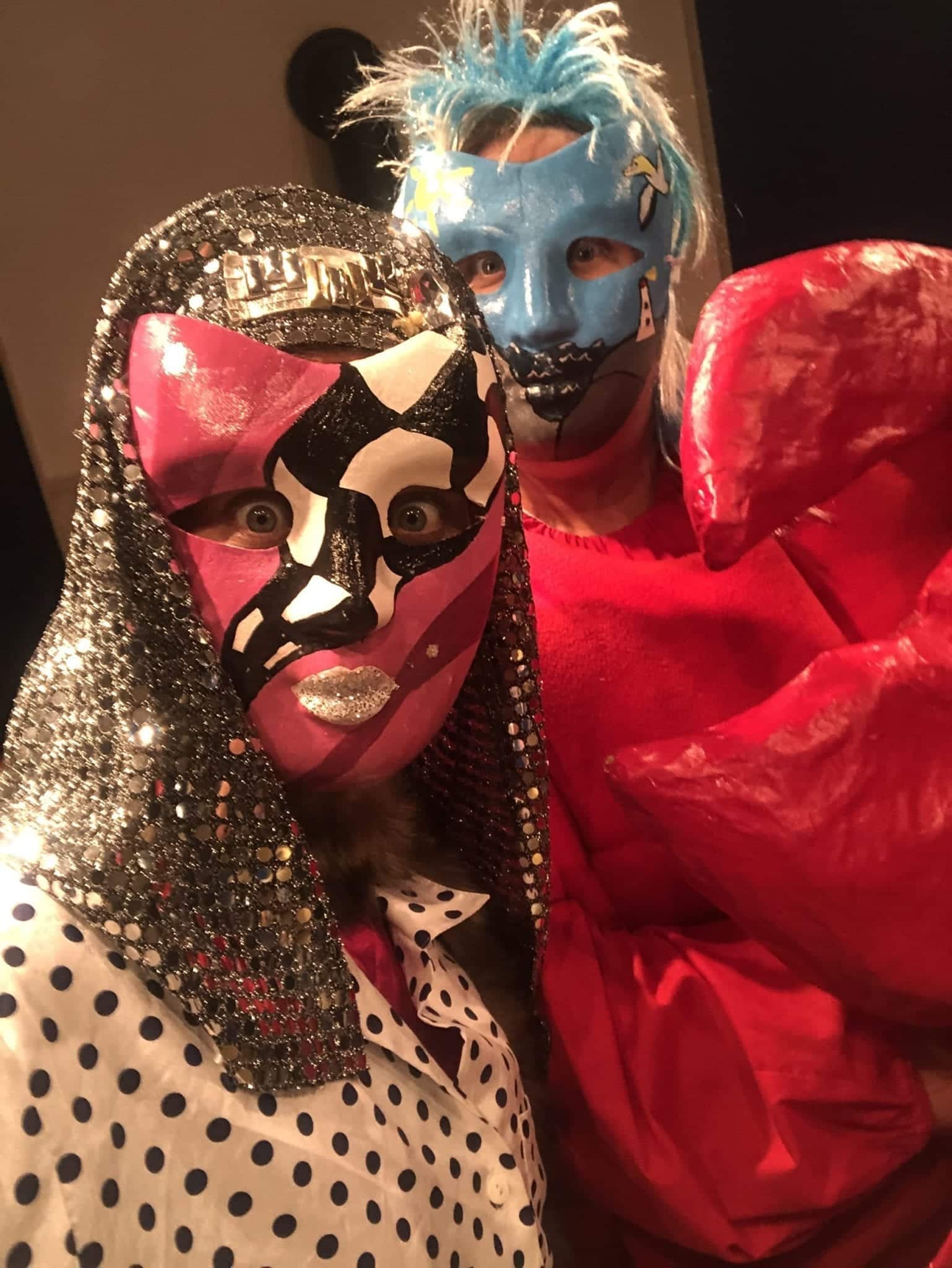 Kate wears a pink and black and white mask with a silver Egyptian-style head covering and black and white spotted top. Cailin wears her Nova Scotia seascape painted mask with a spiky light blue wig while wearing a red lobster costume.