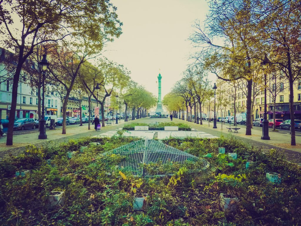 A park running down the center of a Parisian street leading to a tall green column.