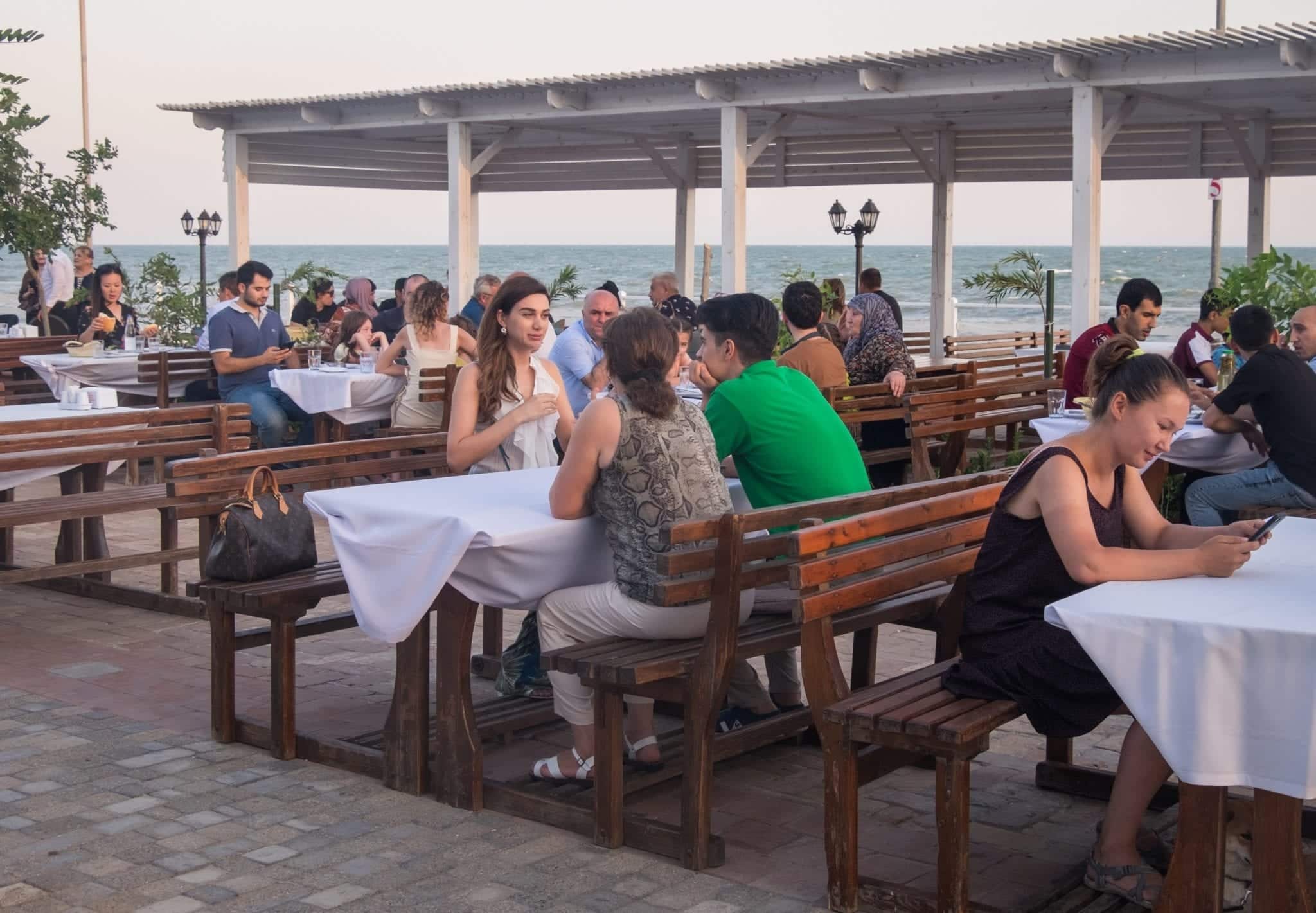 People sitting at outdoor tables at a restaurant on the Caspian Sea.