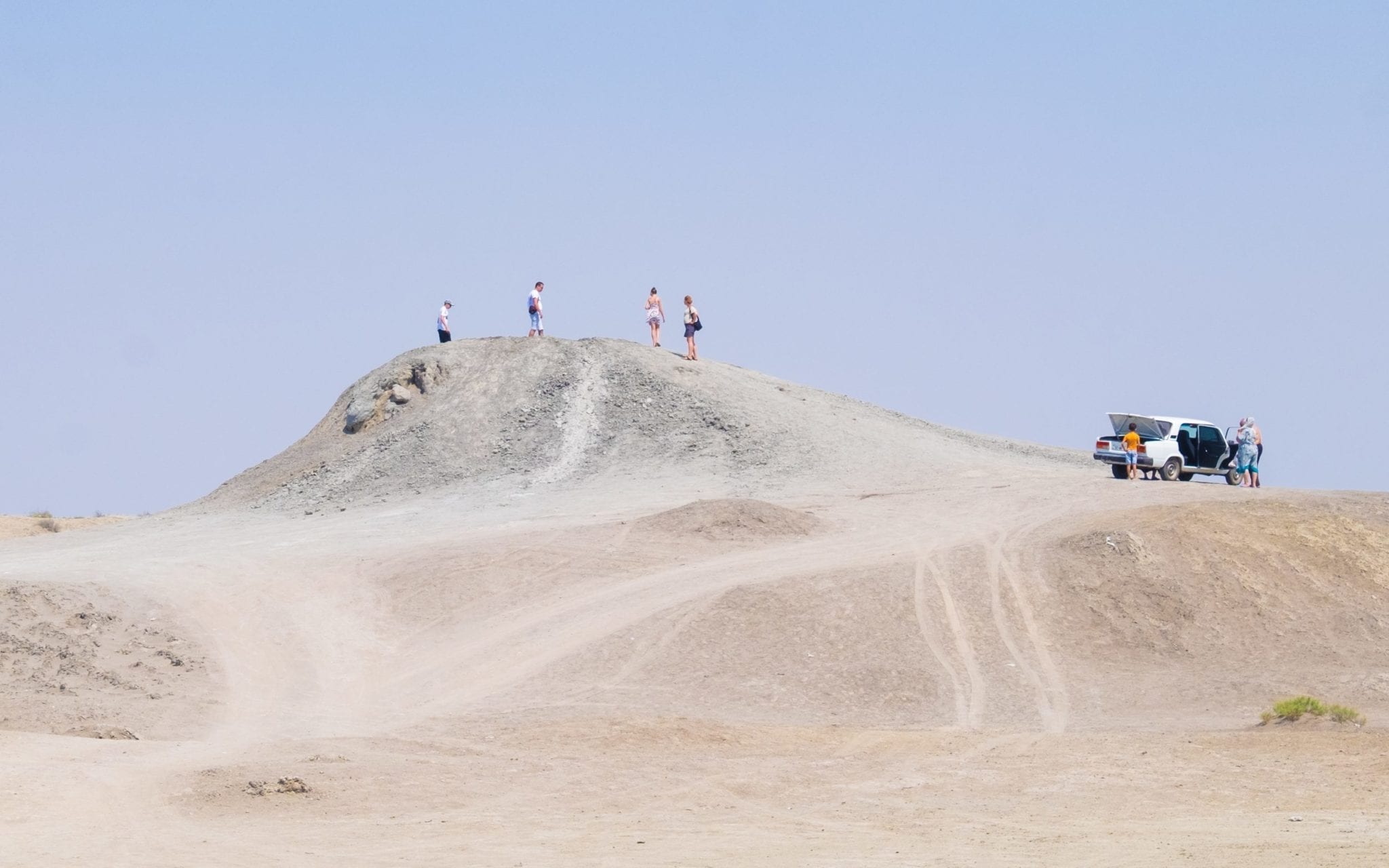  Cuatro diminutas personas de pie sobre un volcán de barro en el desierto, lo que lo hace parecer enorme.