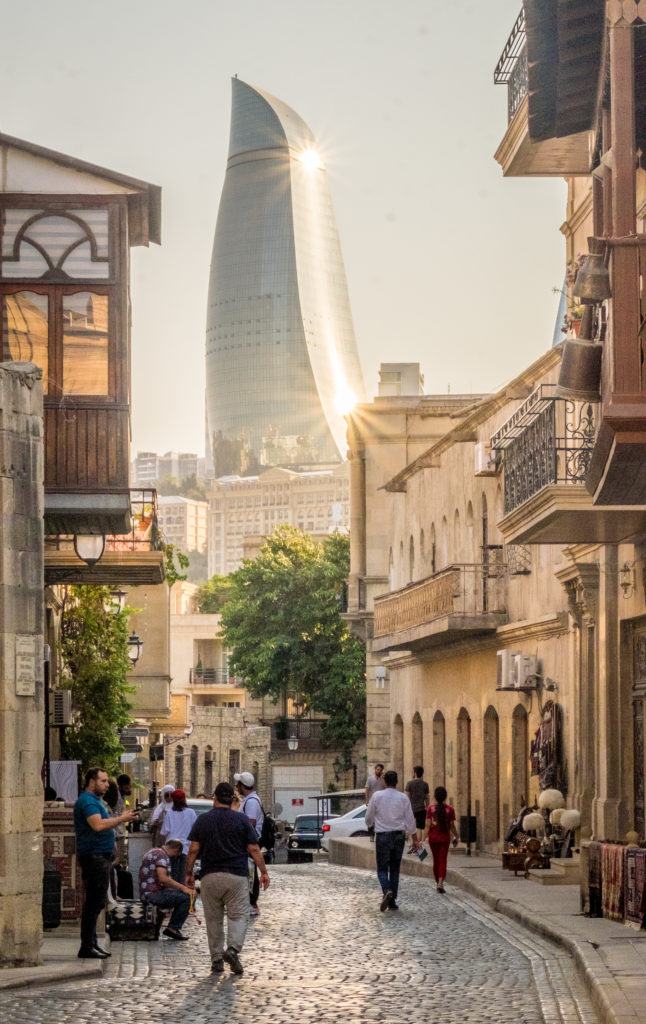 One of the metal Flame Towers of Baku curls in the background; in the foreground is the traditional sand-colored Old Town.