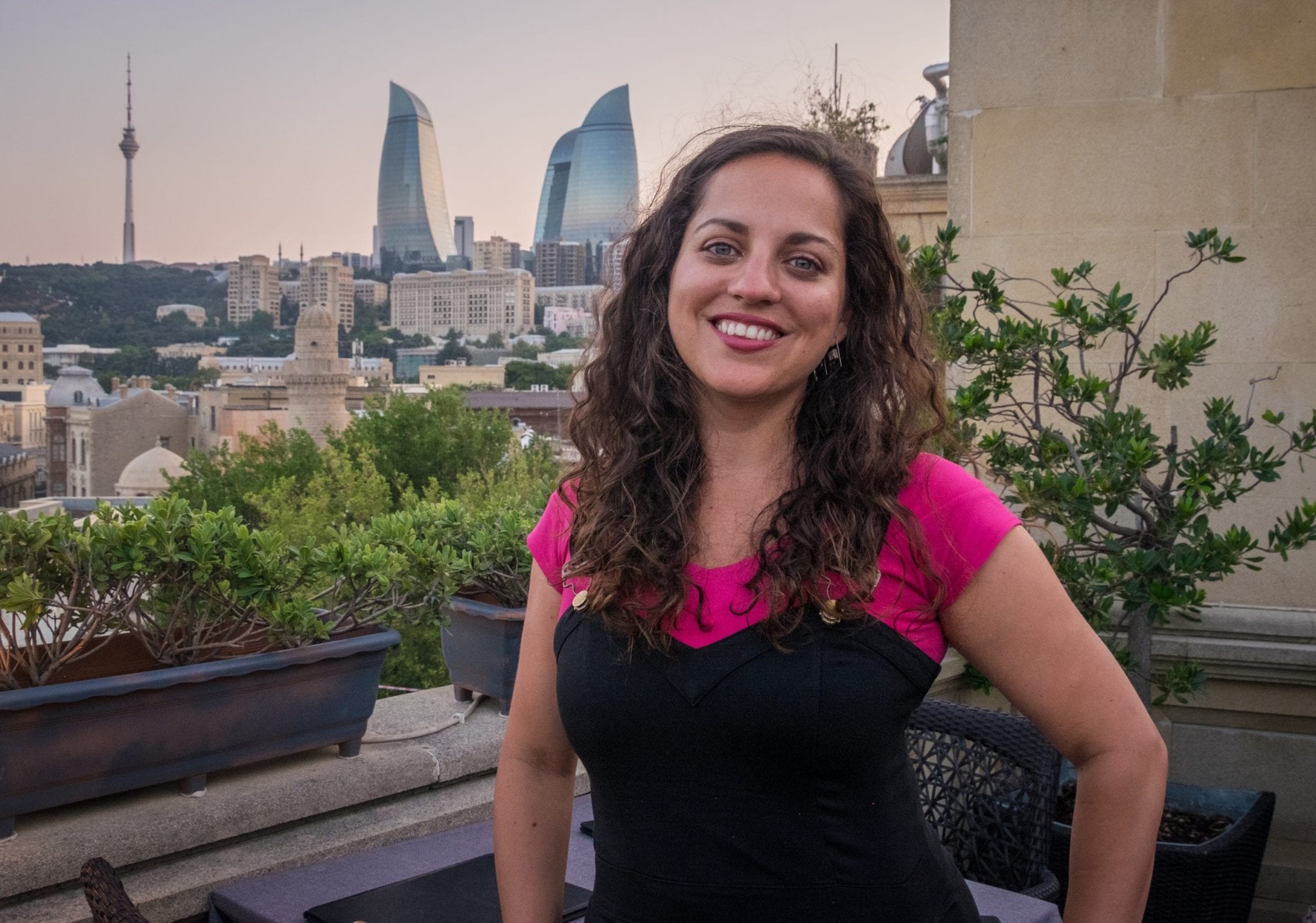 Kate poseert op een balkon voor de drie vlamvormige torens van Azerbeidzjan terwijl de hemel bij zonsondergang roze wordt.