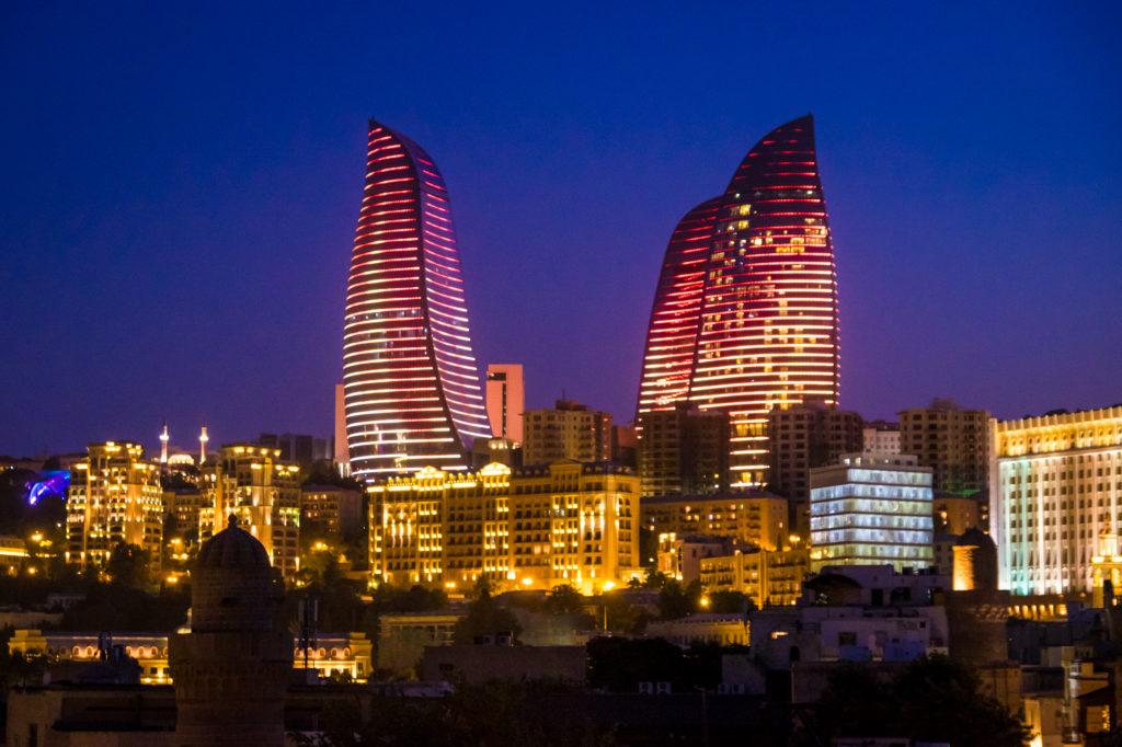 The flame towers of Baku, Azerbaijan, at night: the sky is dark blue and the towers illuminate with red and yellow flames snaking up the building.