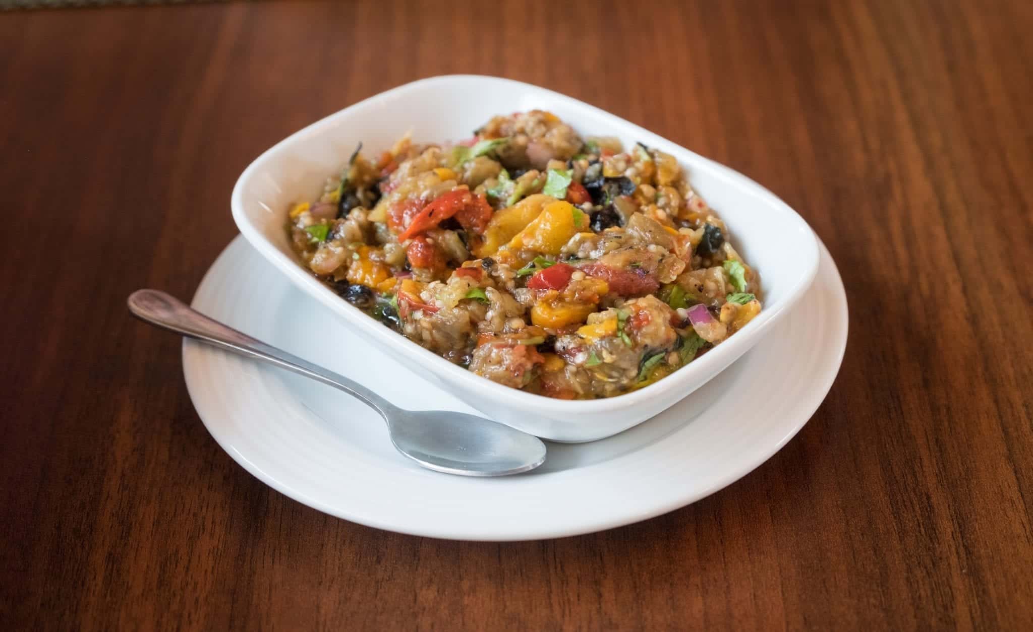 A dish filled with Azerbaijani eggplant caviar, roasted eggplant, peppers, and tomatoes in a dip.