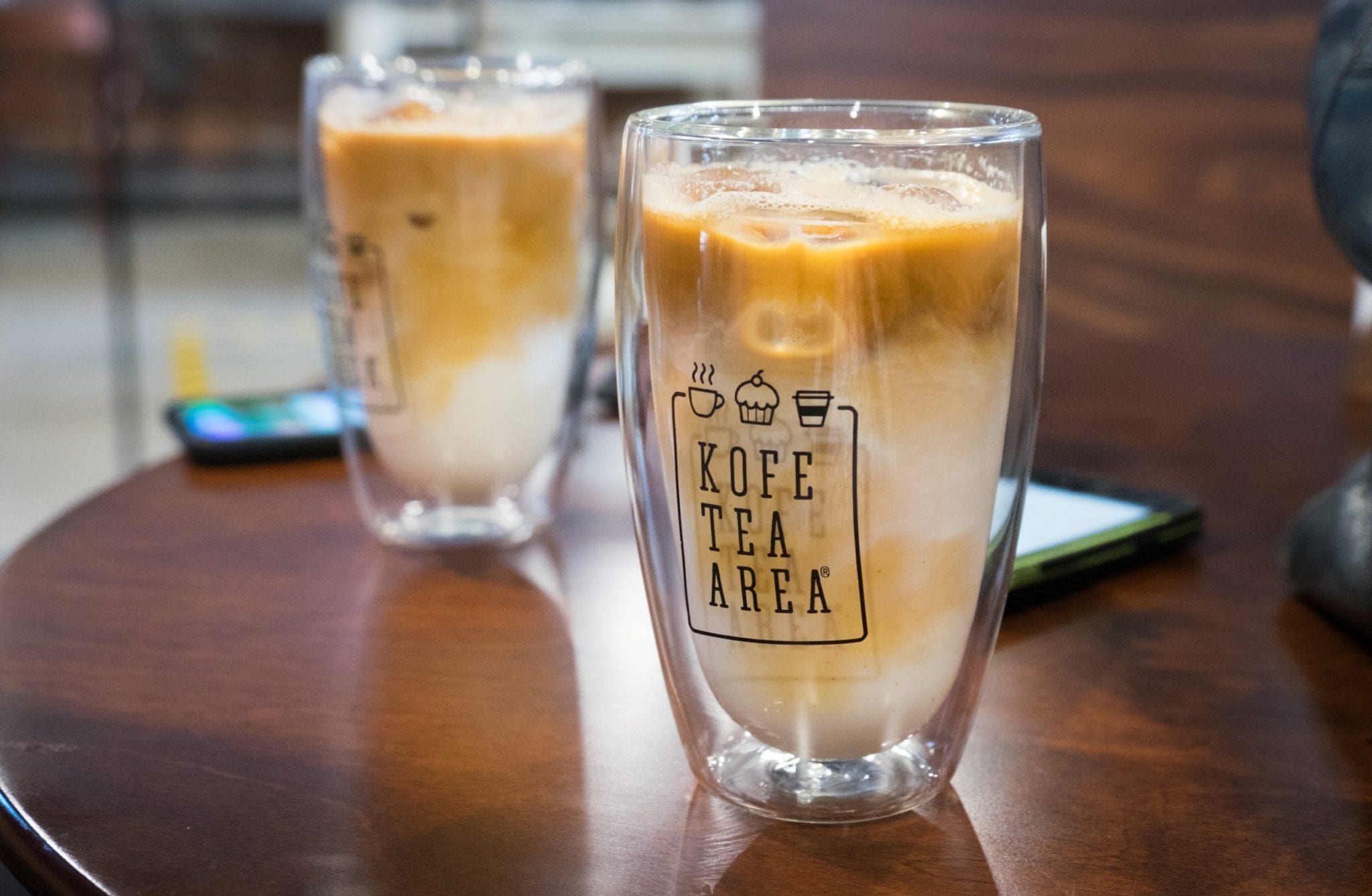  Deux grands lattes en plastique transparent avec le lait et le café tourbillonnant ensemble, entourés de glace.