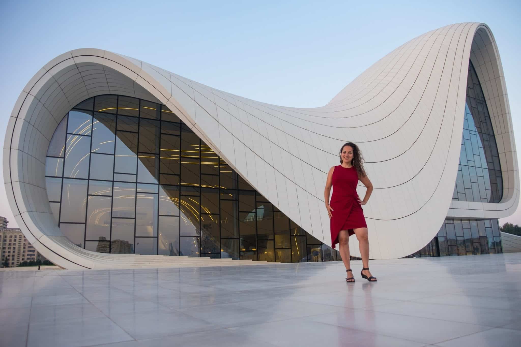 Kate poses in a red dress in front of the white swooping curvy roof and glass wall of the Heydar Aliyev Center in Baku, Azerbaijan.