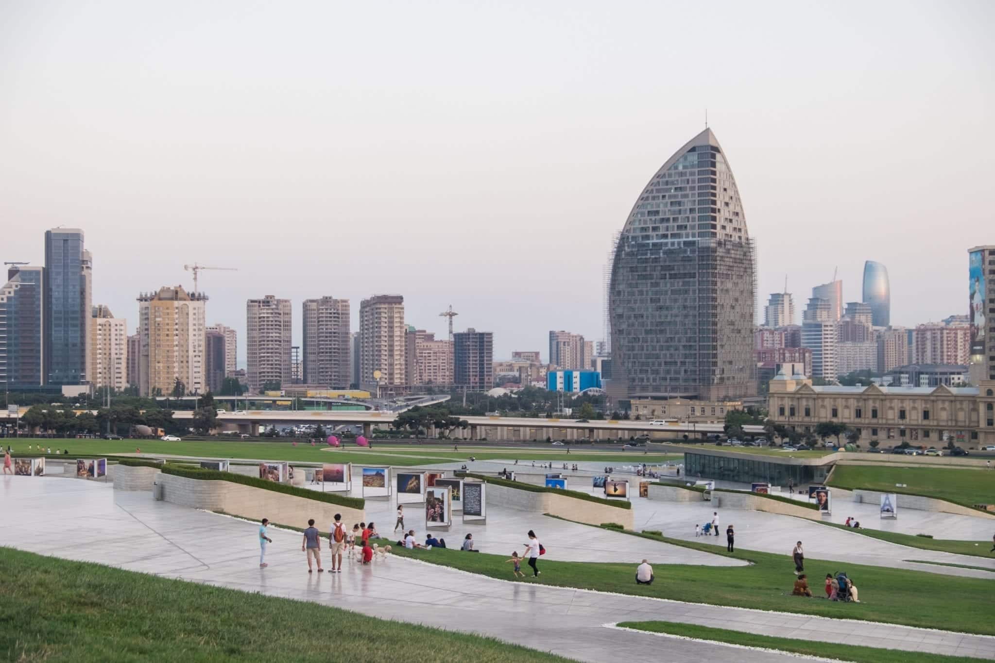  Una serie di moderni edifici grigi di fronte a un grande parco verde con sentieri che lo attraversano.