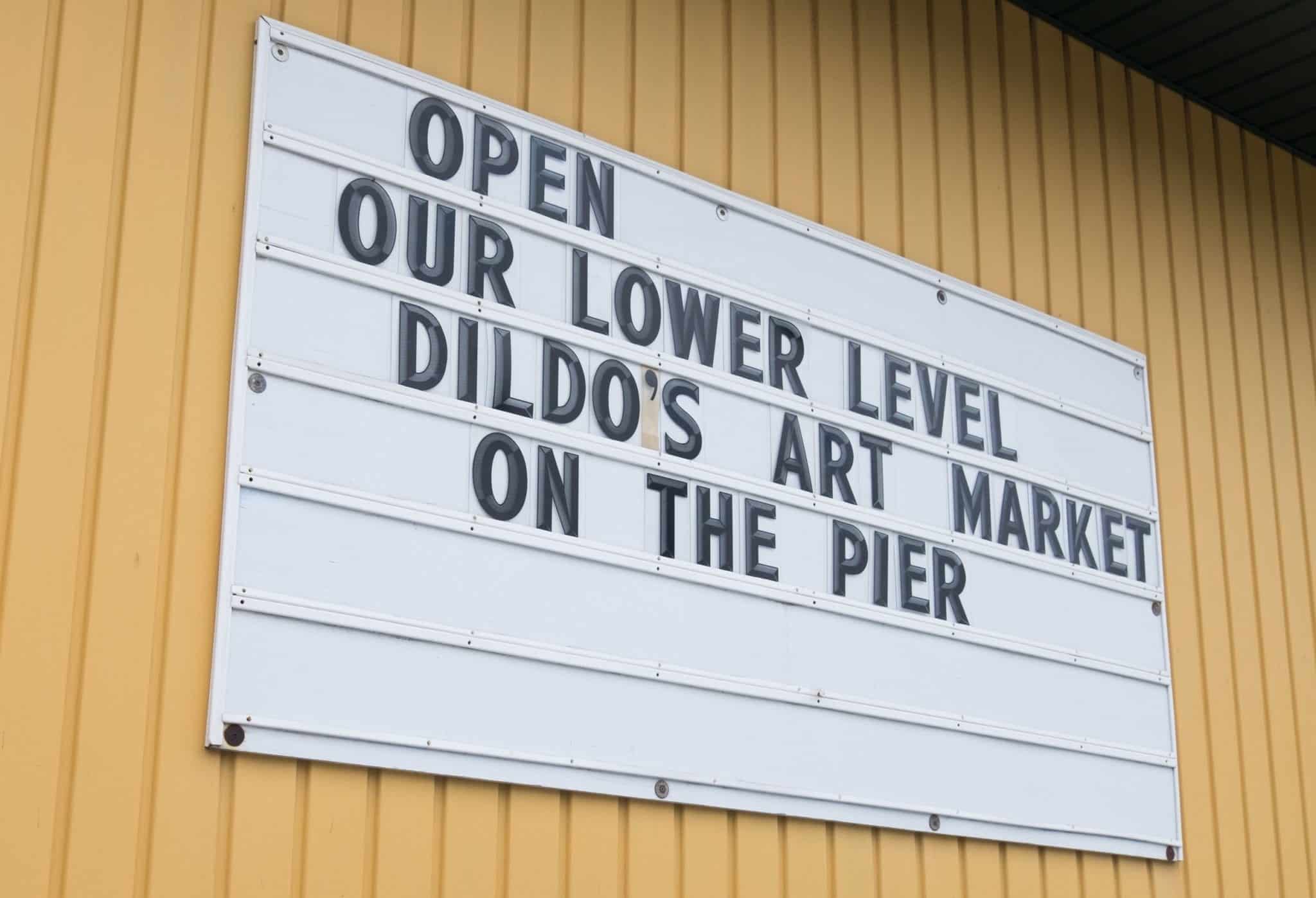 A sign that reads "Open! Our lower level. Dildo's Art Market on the Pier."