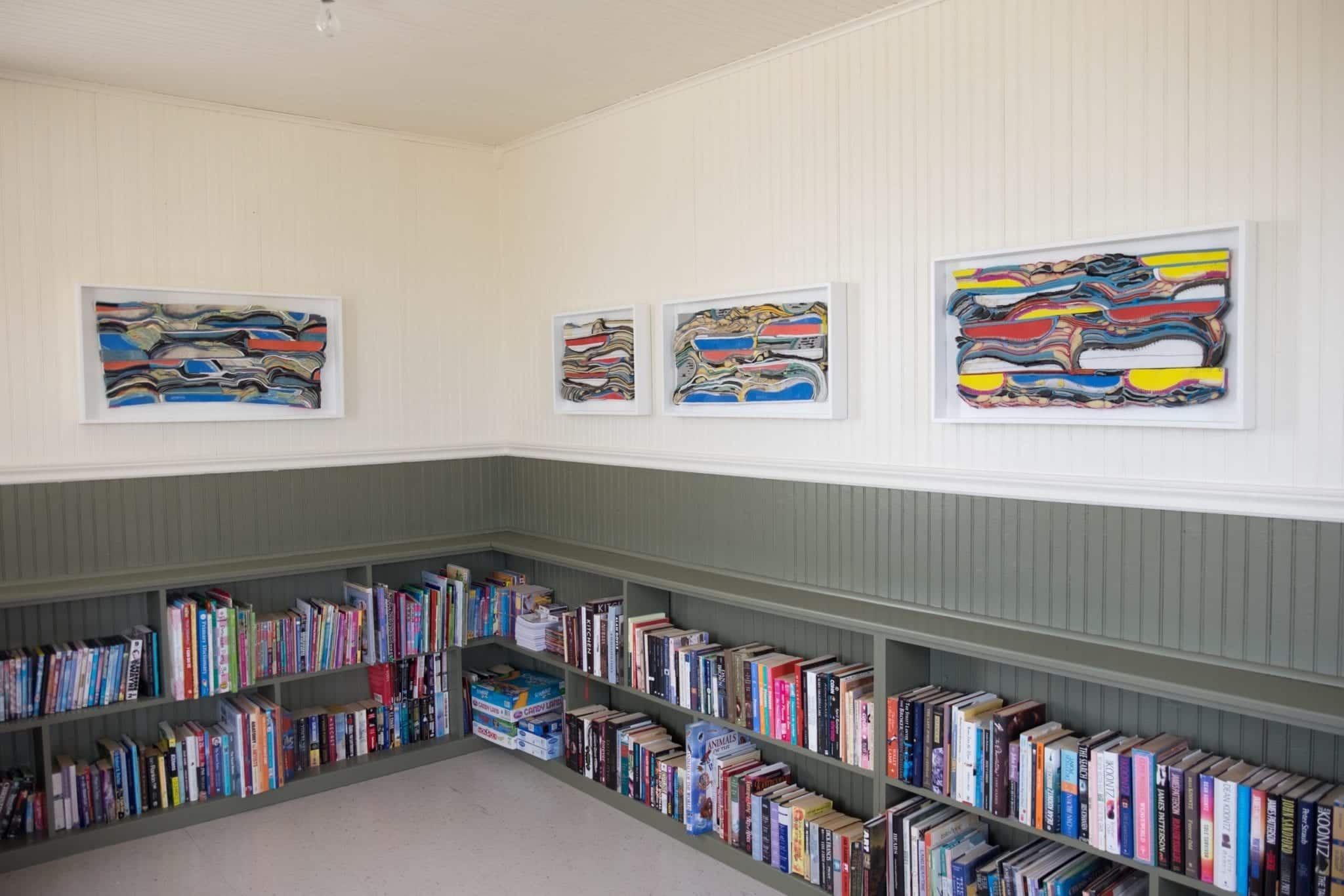 Above low bookshelves, four of Meghan Price's works of art, with the 3d layers of rubber from sneakers symbolizing layers of the Earth's crust.