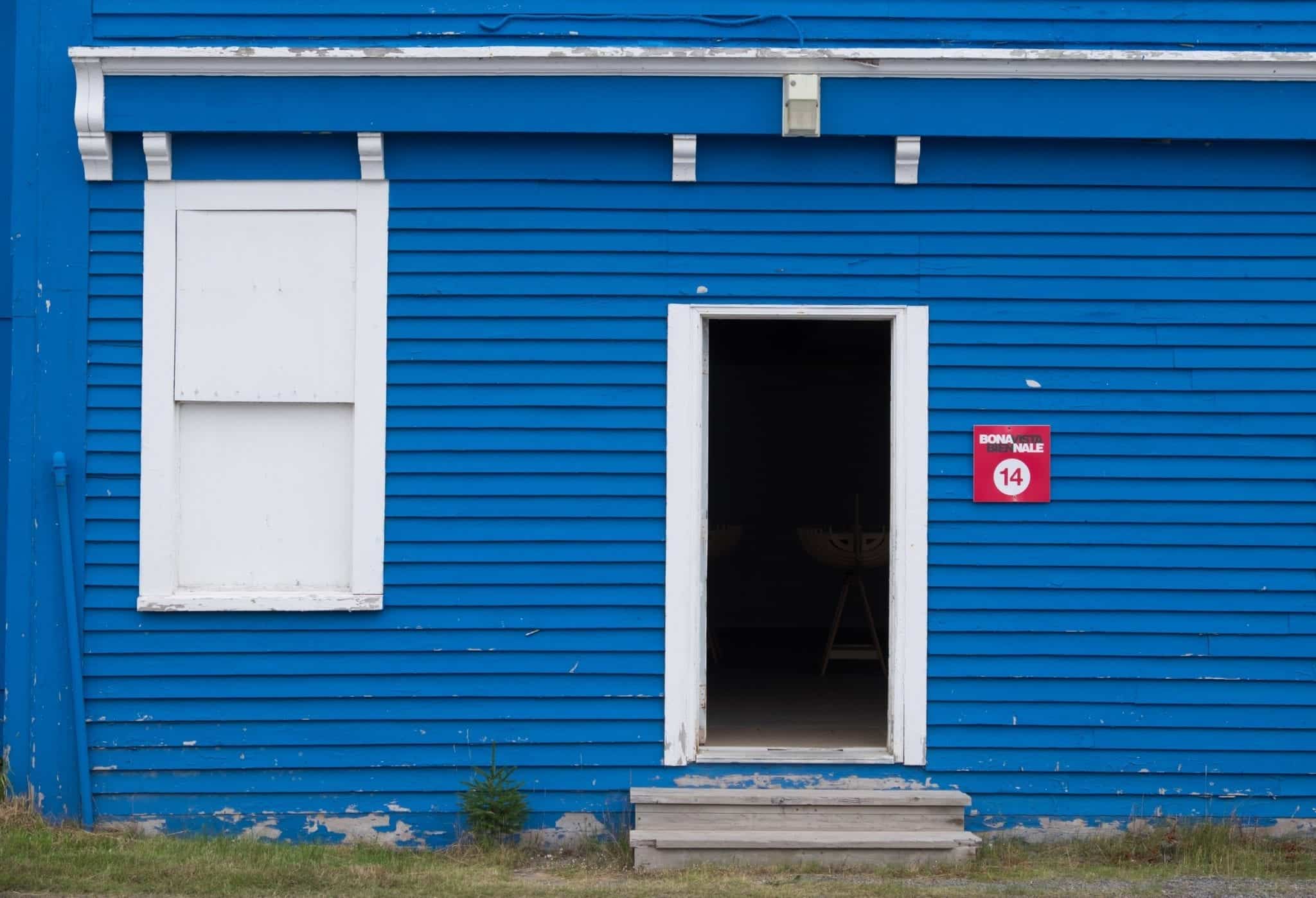 A bright blue building with a red "Bonavista Biennale" sign to the right of the door.