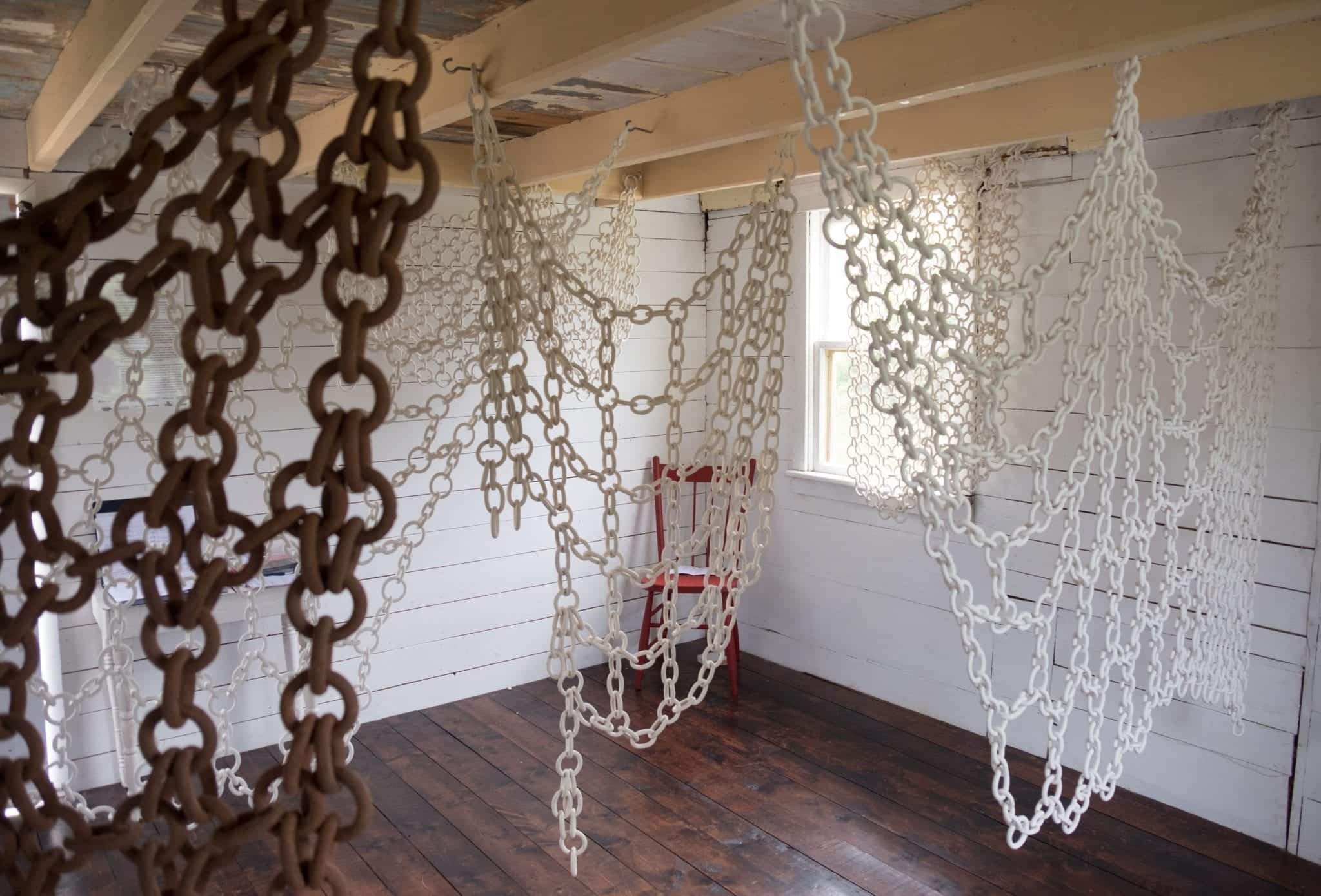 Brown, beige, and white chains made from clay hang in a white room,