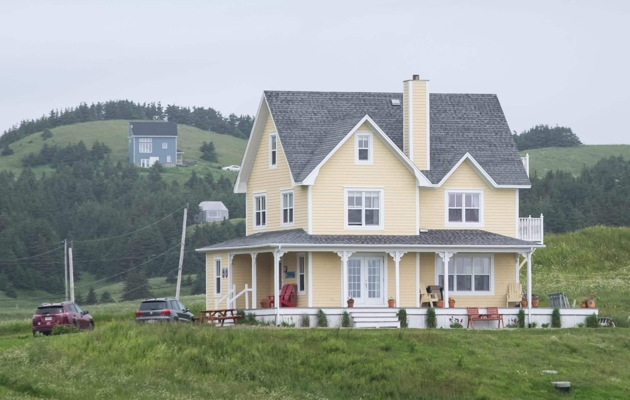 A large pale yellow house with a wraparound porch perched on a hill in the Iles-de-la-Madeleine.