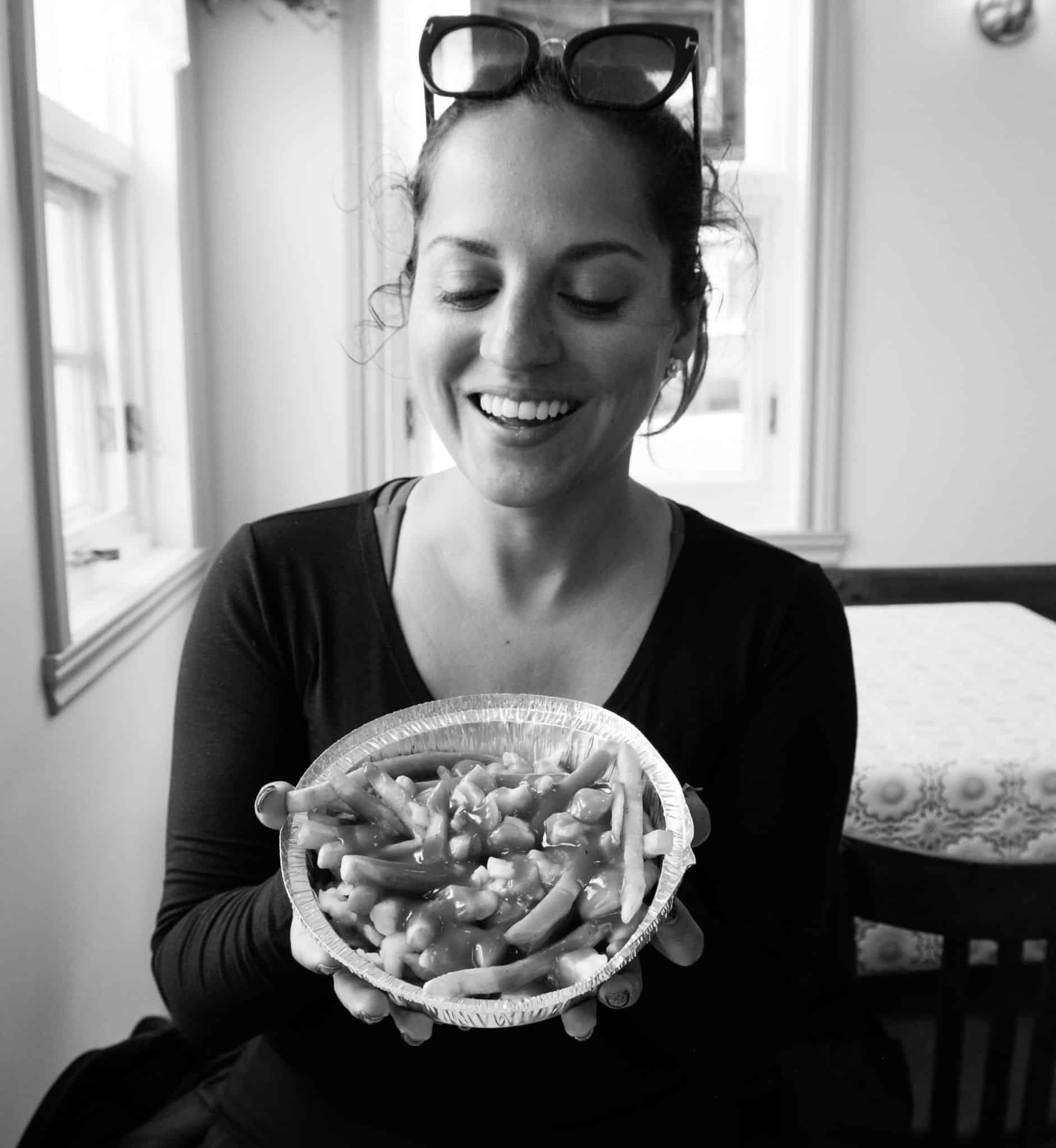 Kate smiles and holds up a bowl of poutine in the Iles-de-la-Madeleine.