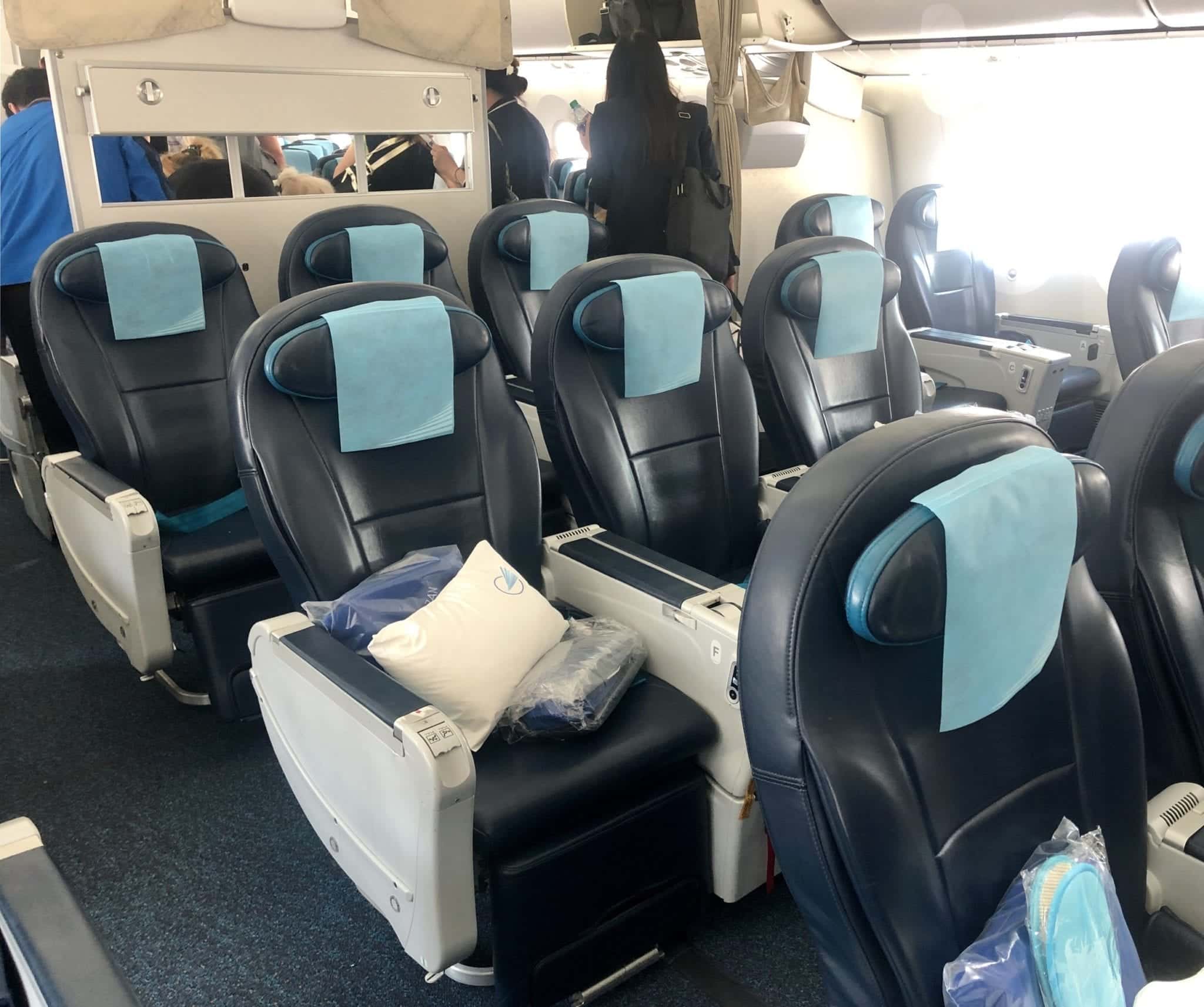 Inside view of an Azerbaijan Airlines flight, Comfort Club. Larger dark blue metal seats separated by thick armrests with pillows and blankets.