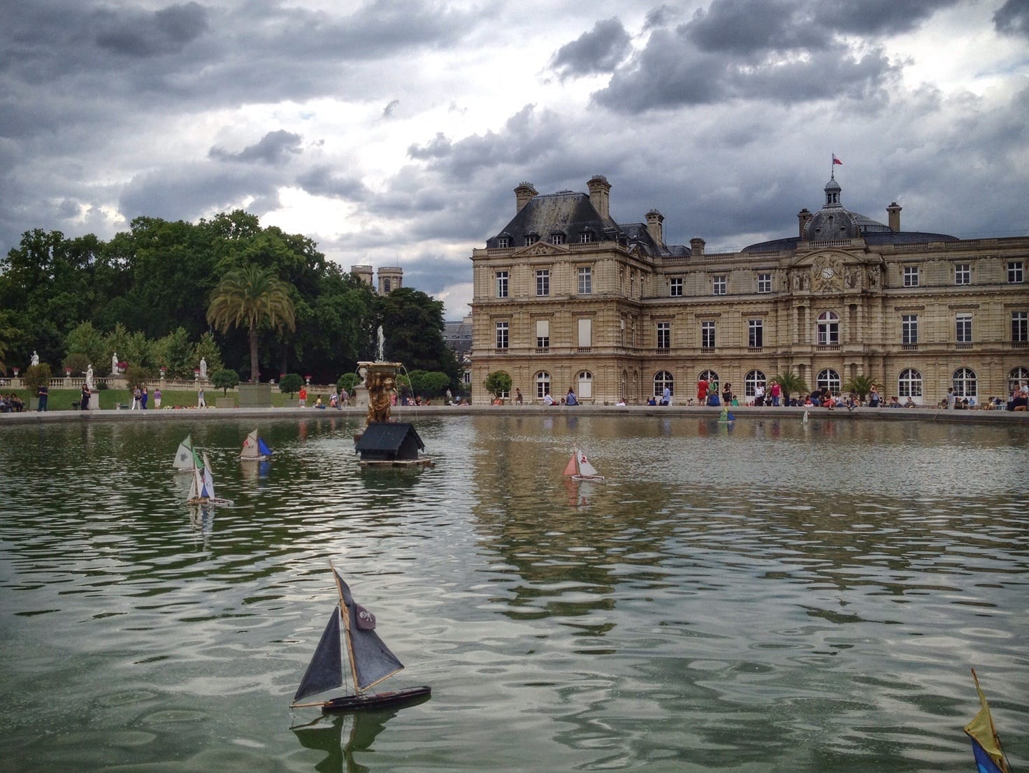 What are the best neighborhoods in Paris? A view of the pond in the Luxembourg Gardens, a sailboat in the water, gray clouds overhead.