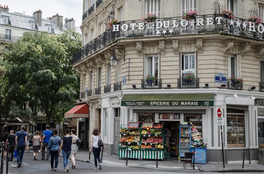 Where to Stay in Paris: a hotel in The Marais, a fruit shop at the base, with people walking by.
