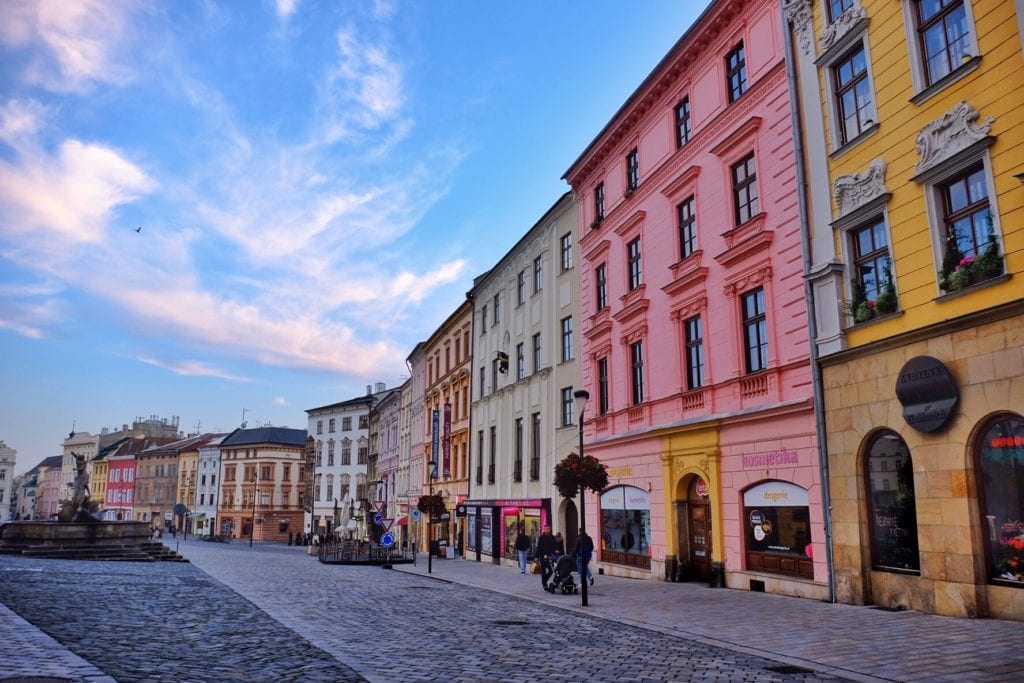Bright pink and yellow buildings of Olomouc set against a bright blue sky.