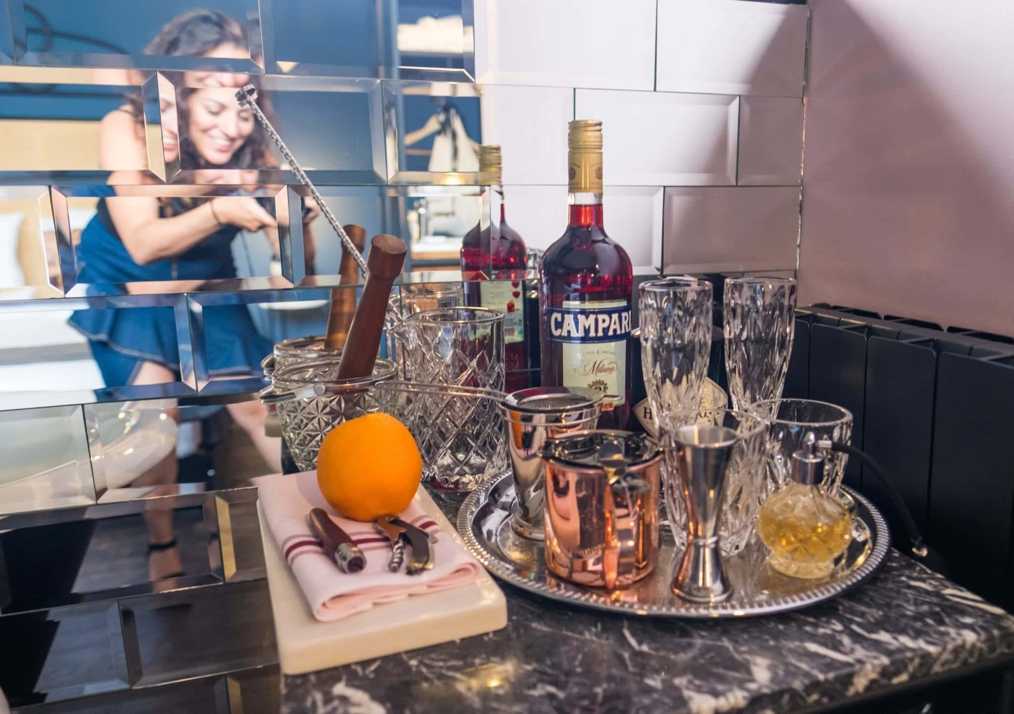 Kate takes a photo of liquor bottles and crystal glasses on a mirrored tray at the Communal Hotel in Tbilisi. You can see her reflection in the mirrored tiles behind her.