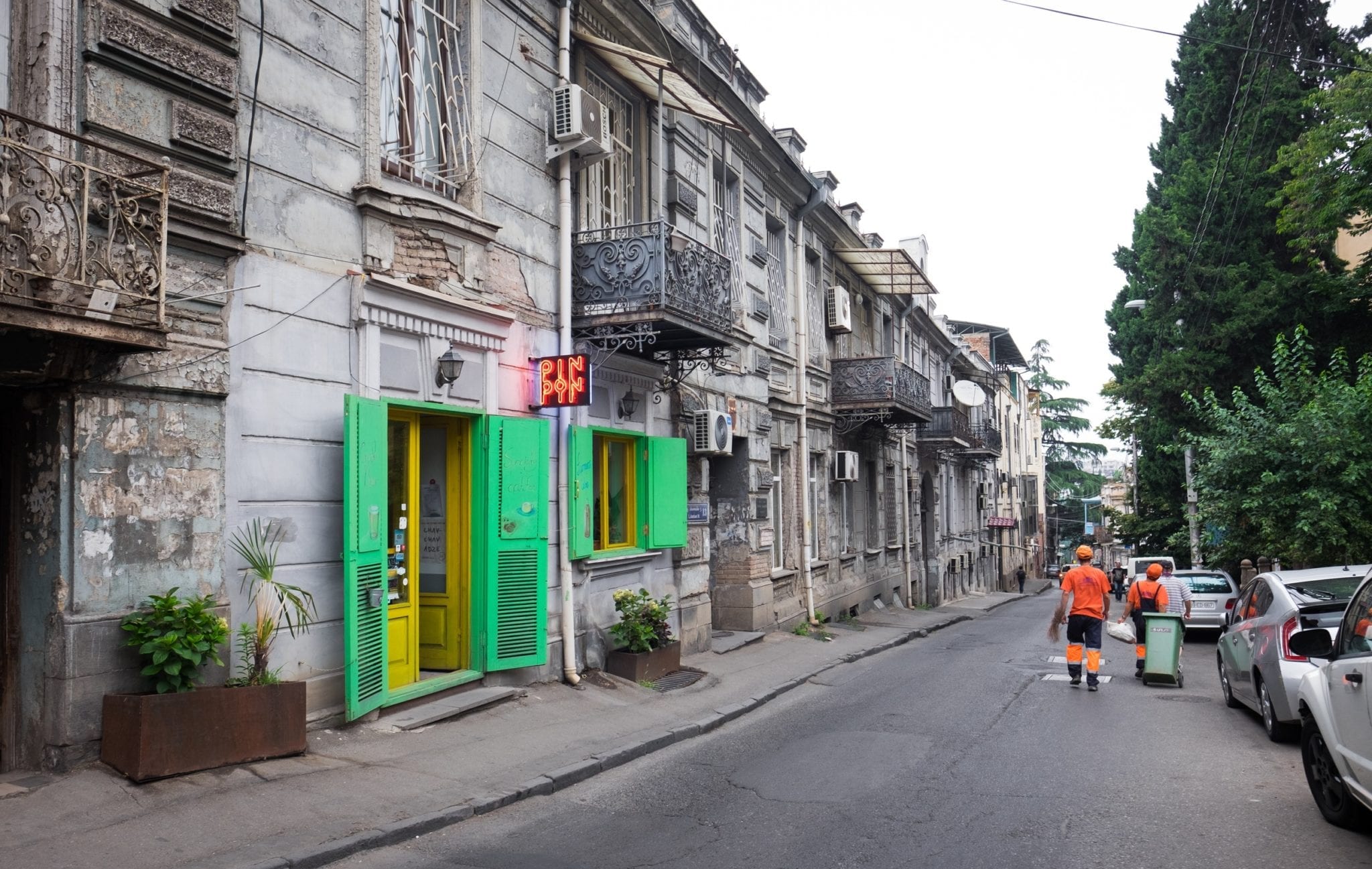 A gray street in Tbilisi interrupted by a bright neon green and yellow coffeeshop.