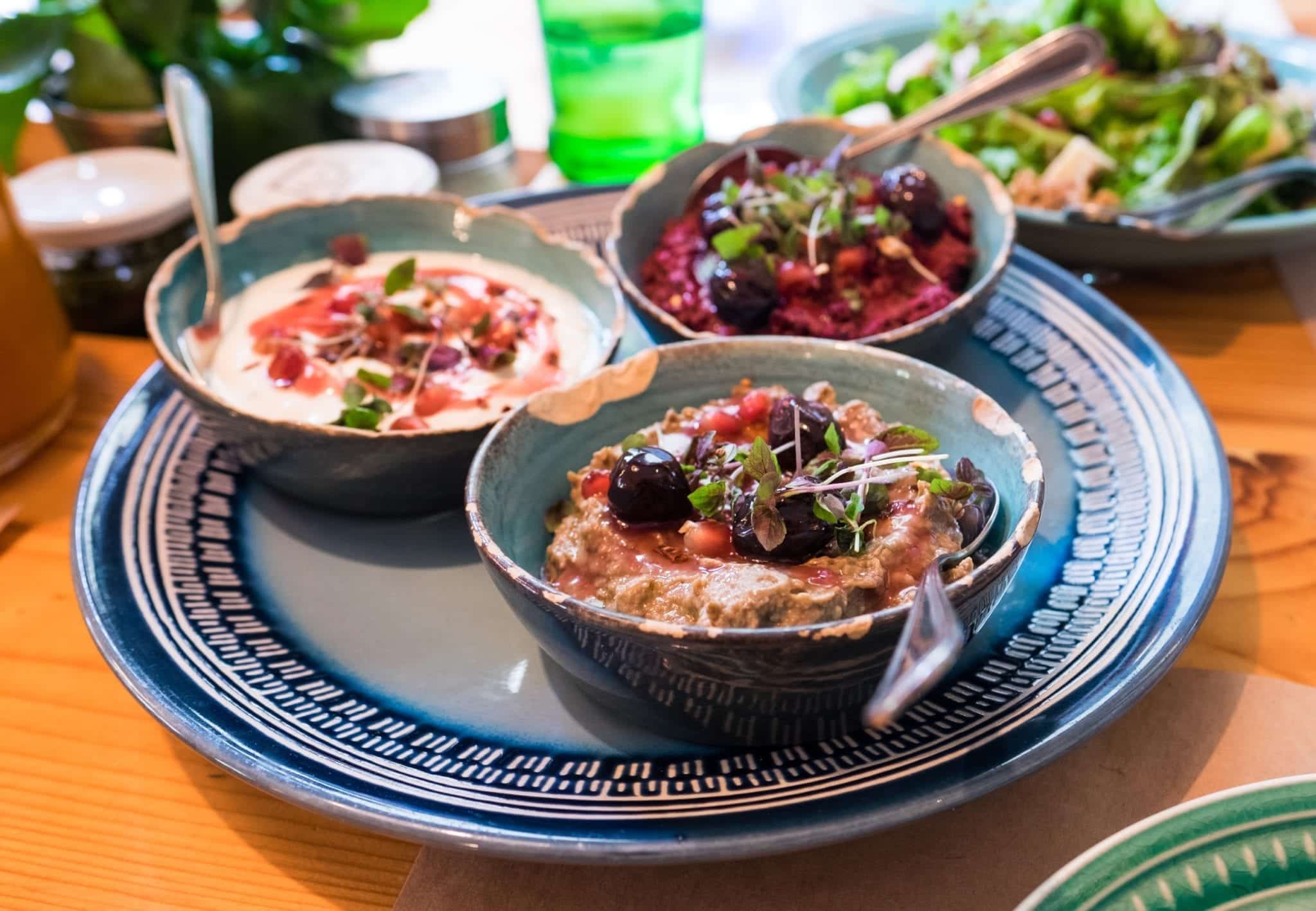 A plate covered with three tiny bowls, each filled with a different kind of Georgian walnut dip, topped with parsley.