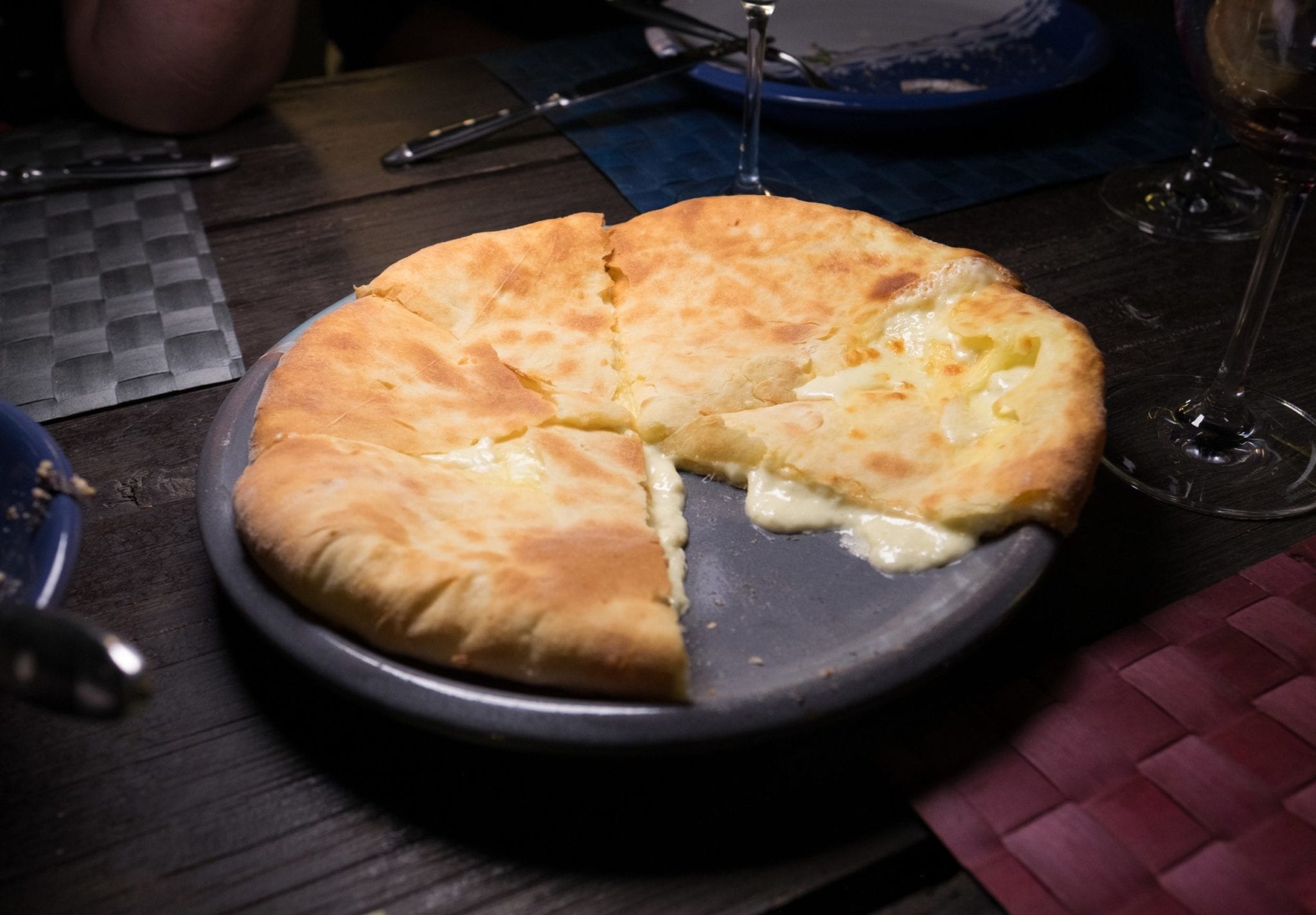 A khachapuri (Georgian cheese pie) with one slice missing, the cheese oozing out.