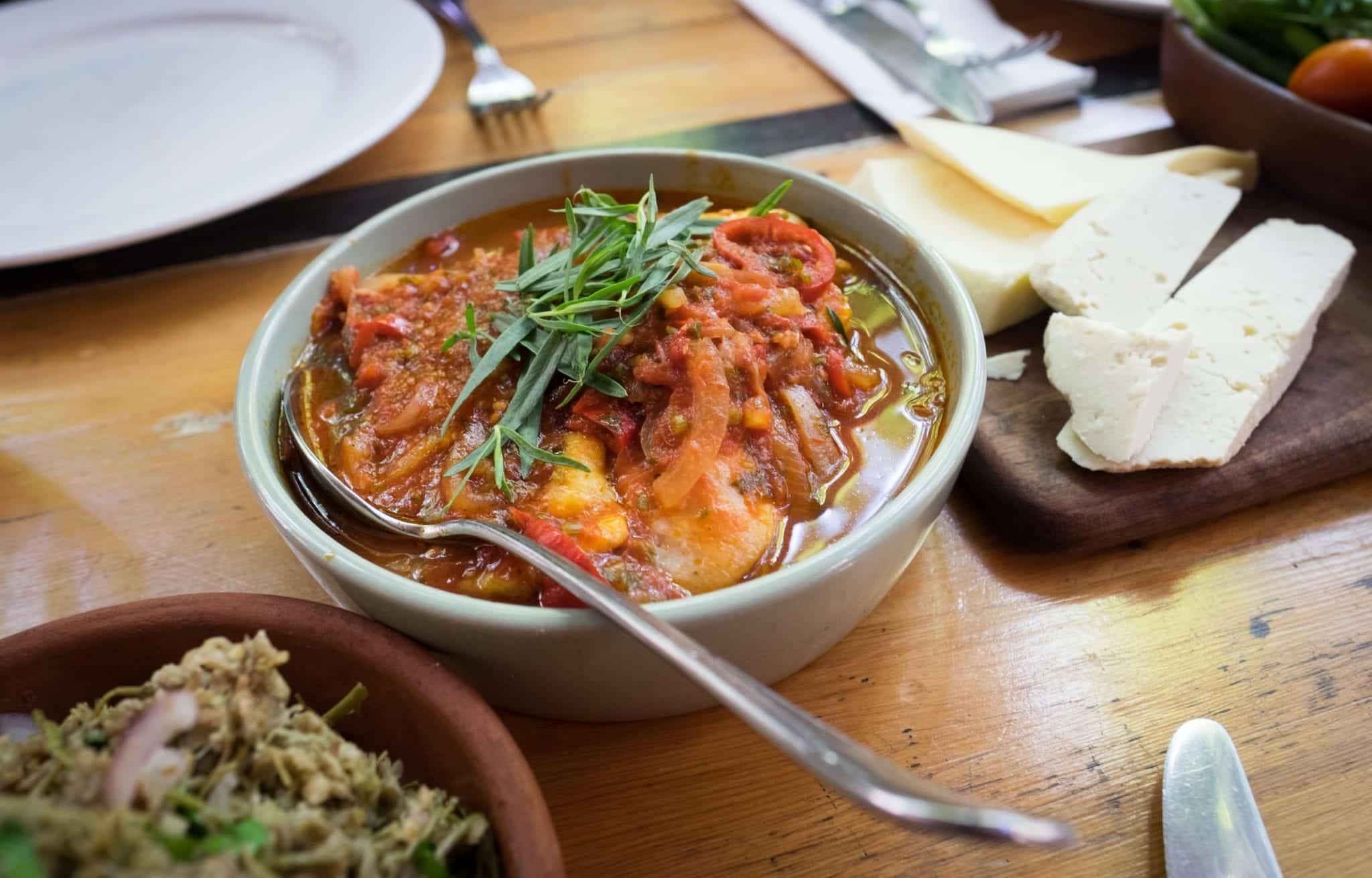 A bowl filled with chicken, tomatoes and onions and topped with a spring of rosemary.