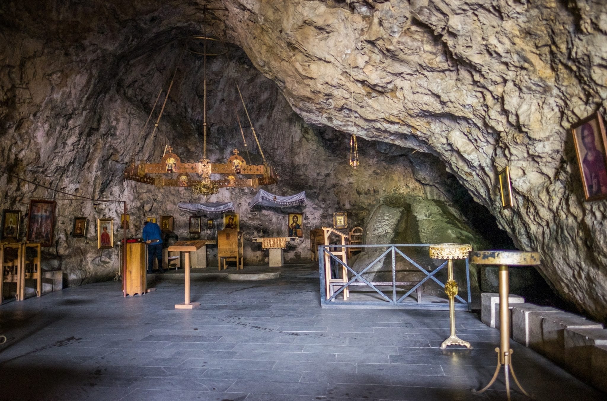 A cave monastery, with a religious altar in the back of a cave and golden tables placed around it.