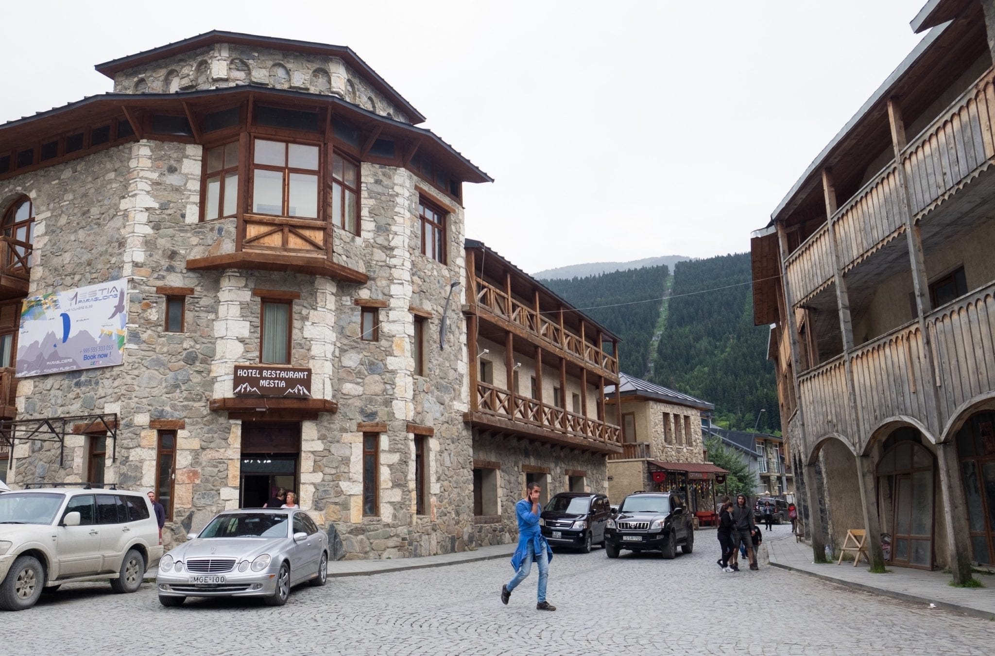 A man walking across the street surrounded by stone-and-wood buildings in Mestia town.