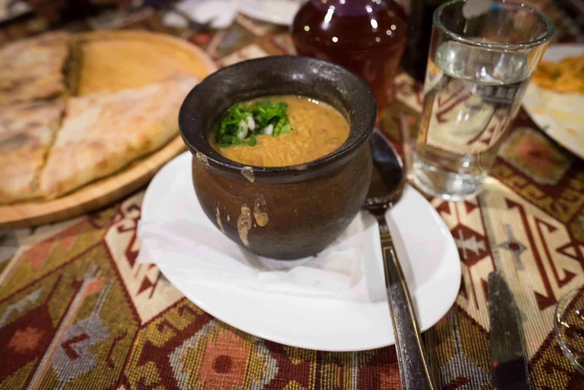A dark brown vase-like bowl filled with lobio, Georgian stewed beans, sitting on a white plate.