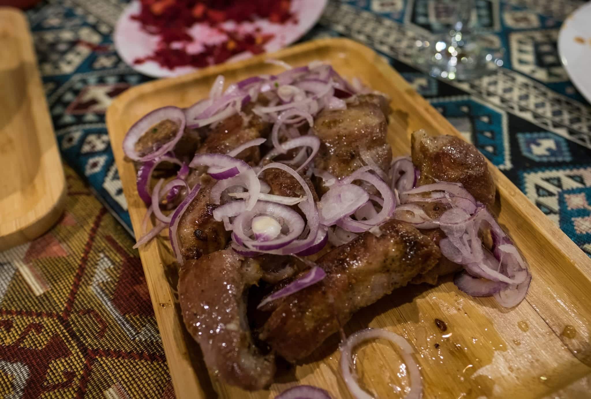 A wooden platter topped with (probably overcooked) pork strips, topped with raw red onions.