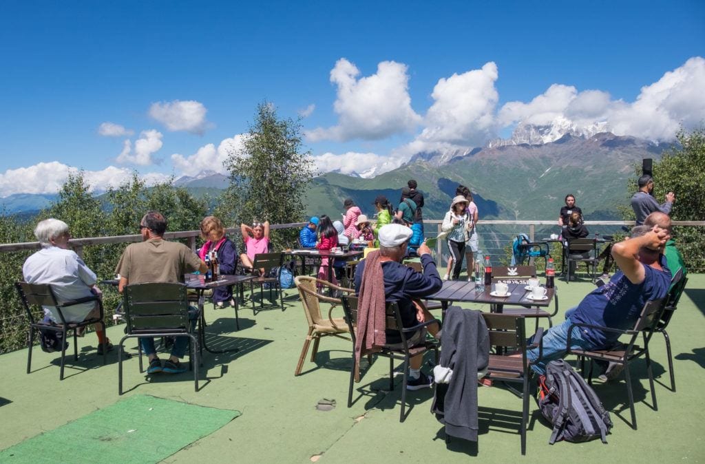 People eating outside at tables on a patio overlooking the mountains of Svaneti.