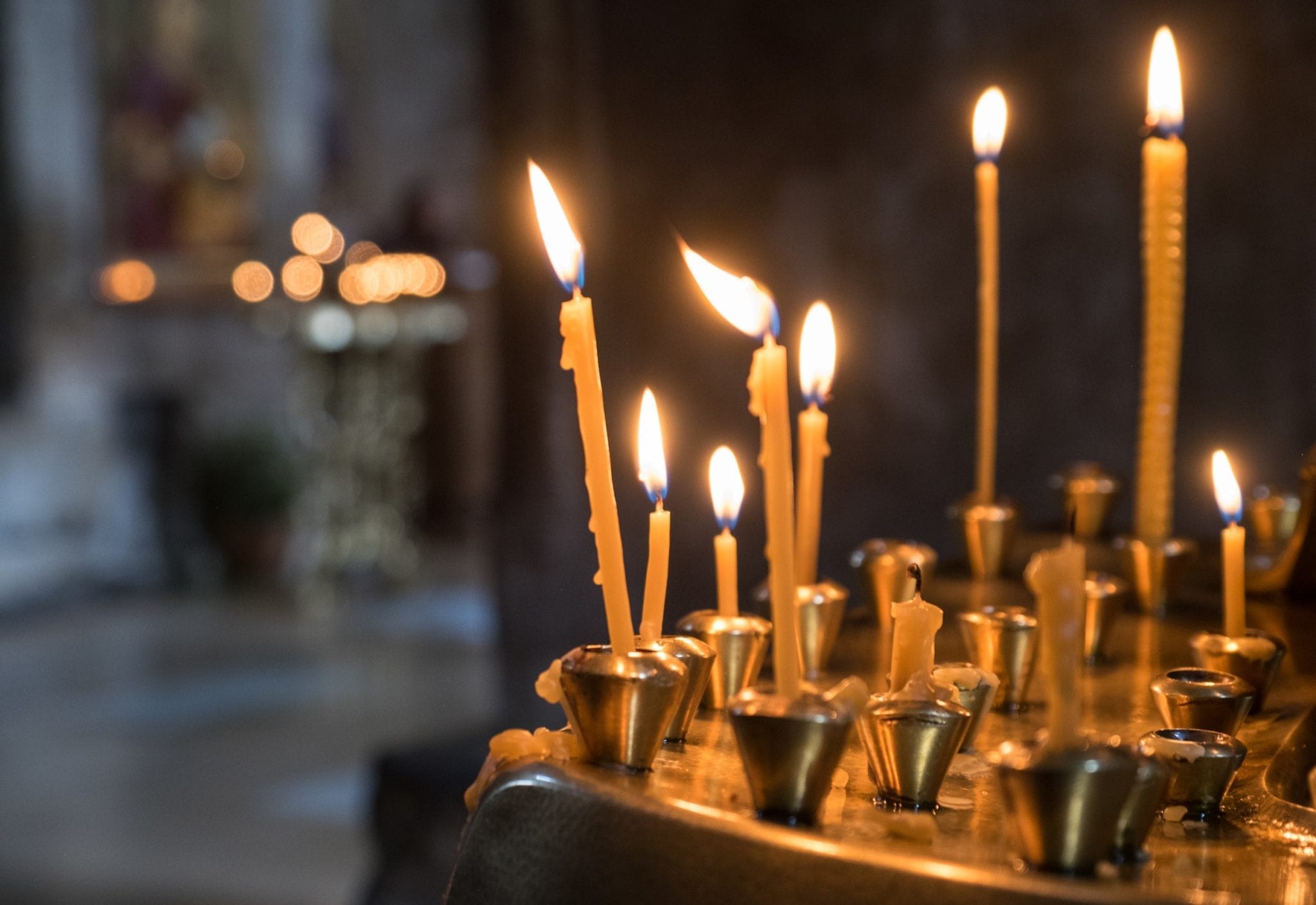 Tall, skinny yellow candles burning on a gold offering table in a church in Mtskheta, Georgia.