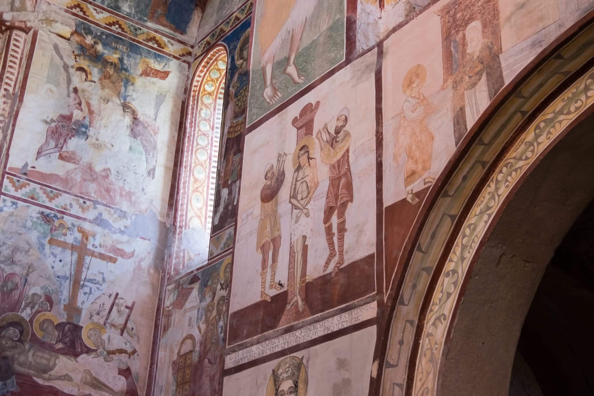 Interior of Gelati Monastery with earth-colored frescoes of sacred scenes in the Bible painted on the walls.