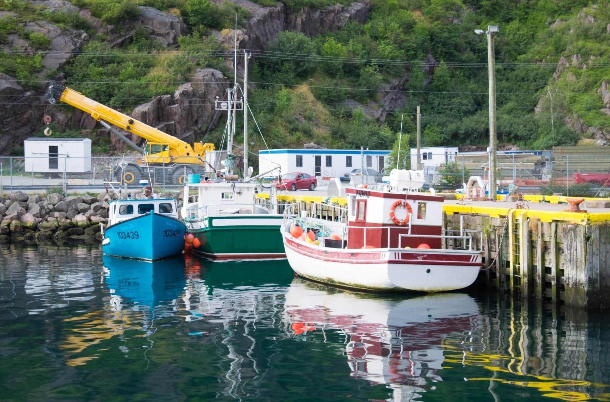 Boats sitting on a glassy teal harbor in Newfoundland.