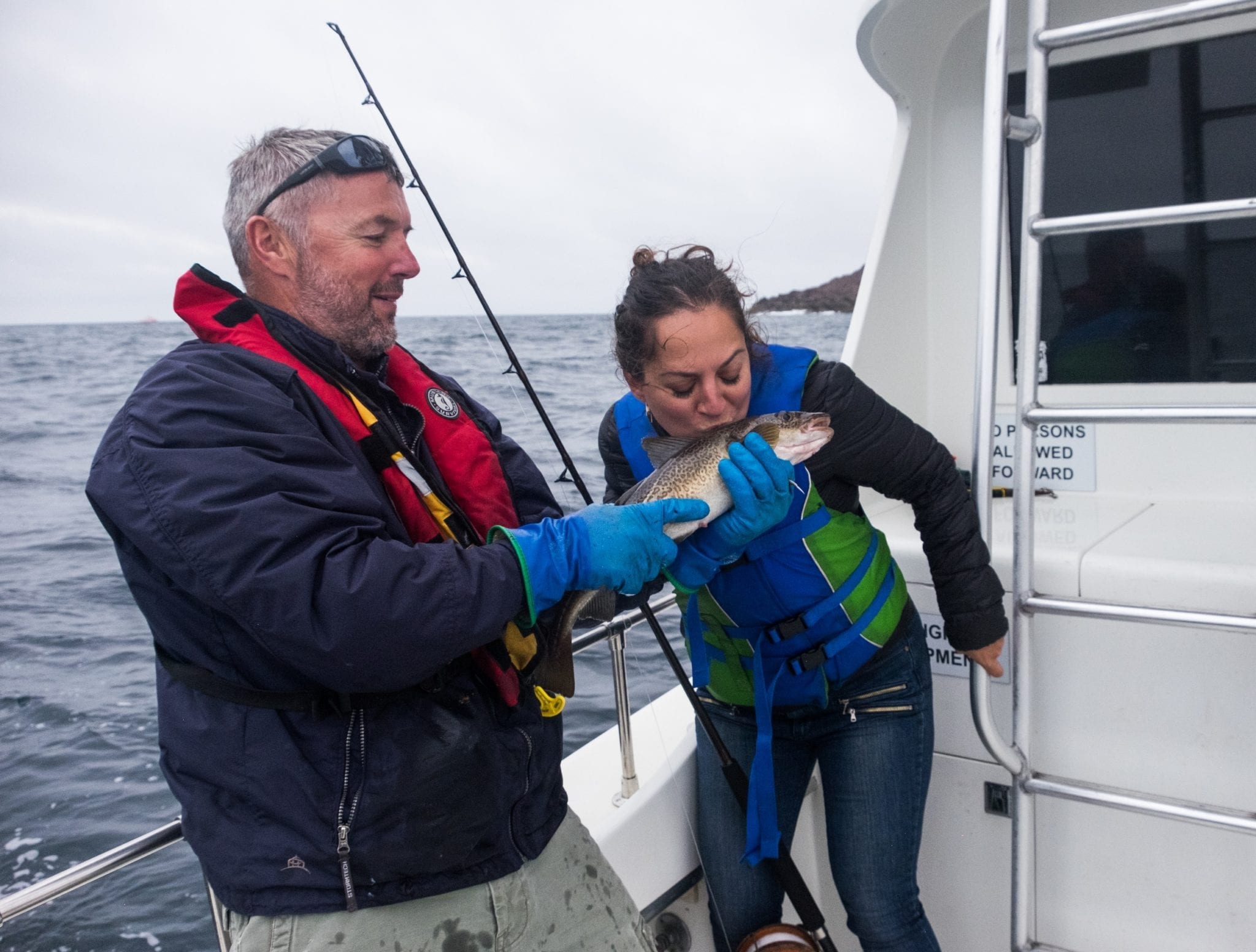 A fisherman holds up a cod for Kate and she leans in and kisses it.