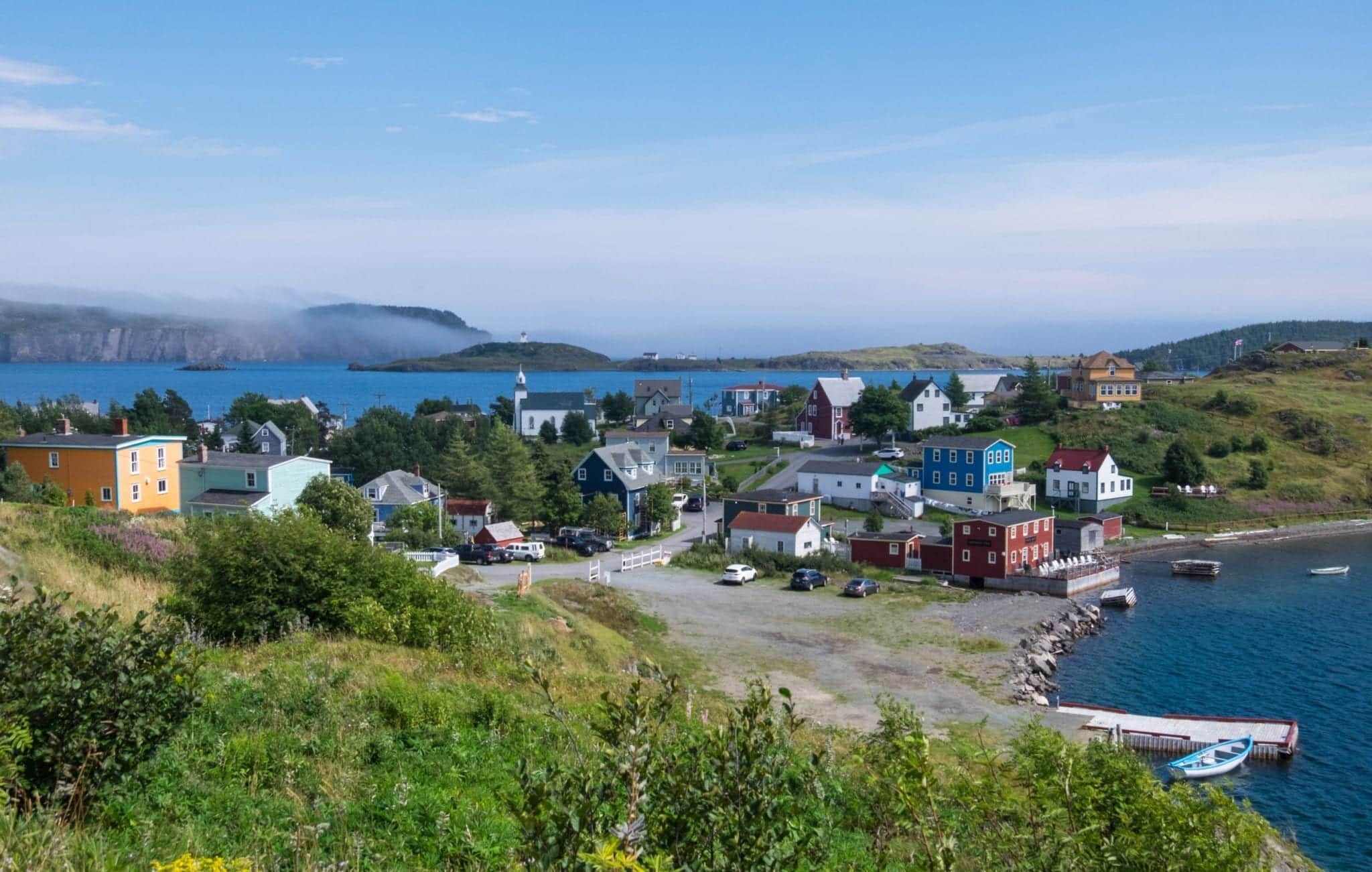 Brightly colored cottages on a grassy peninsula in the distance, surrounded by bright blue water.