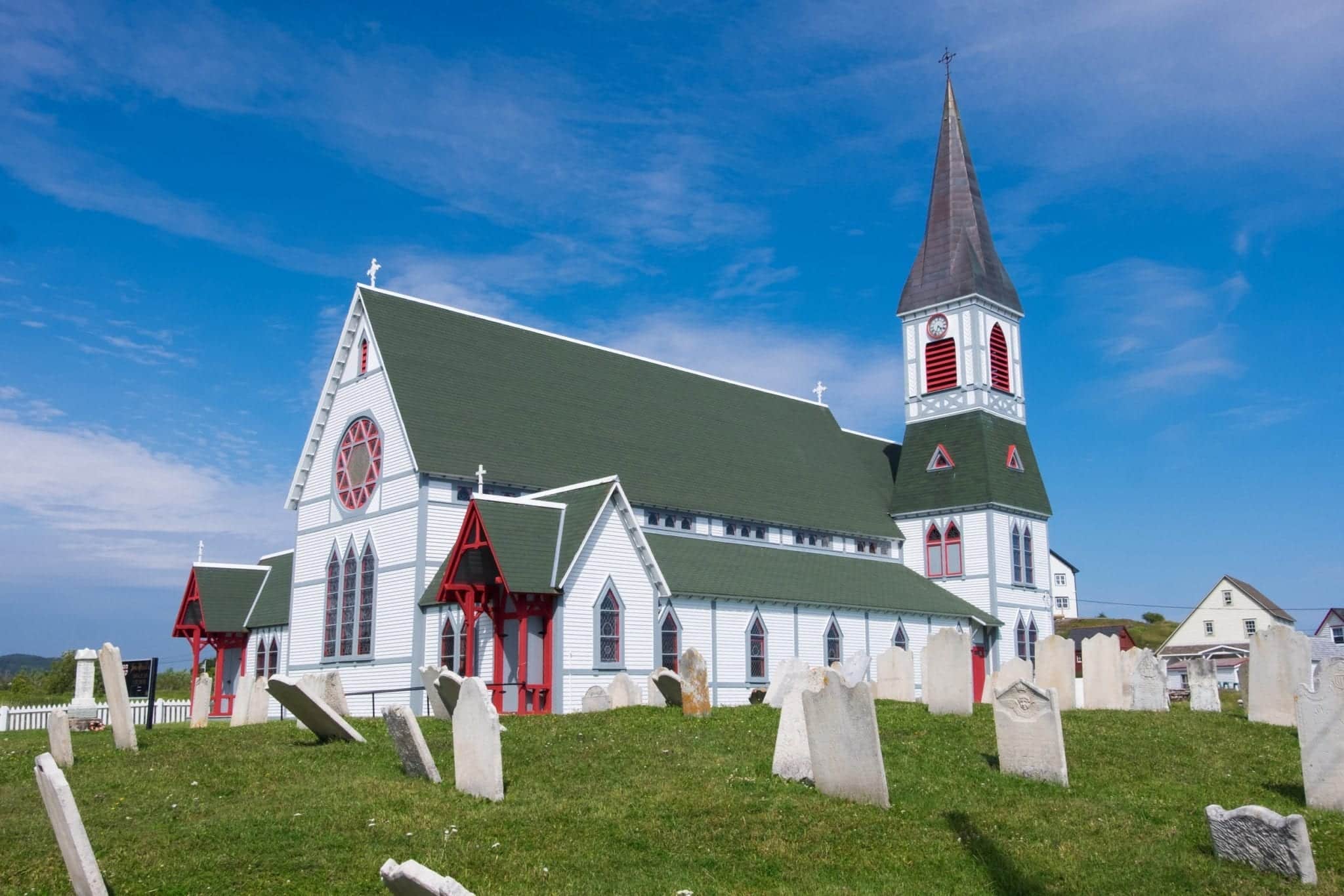 A white church with a green roof and steeple underneath a bright blue sky.