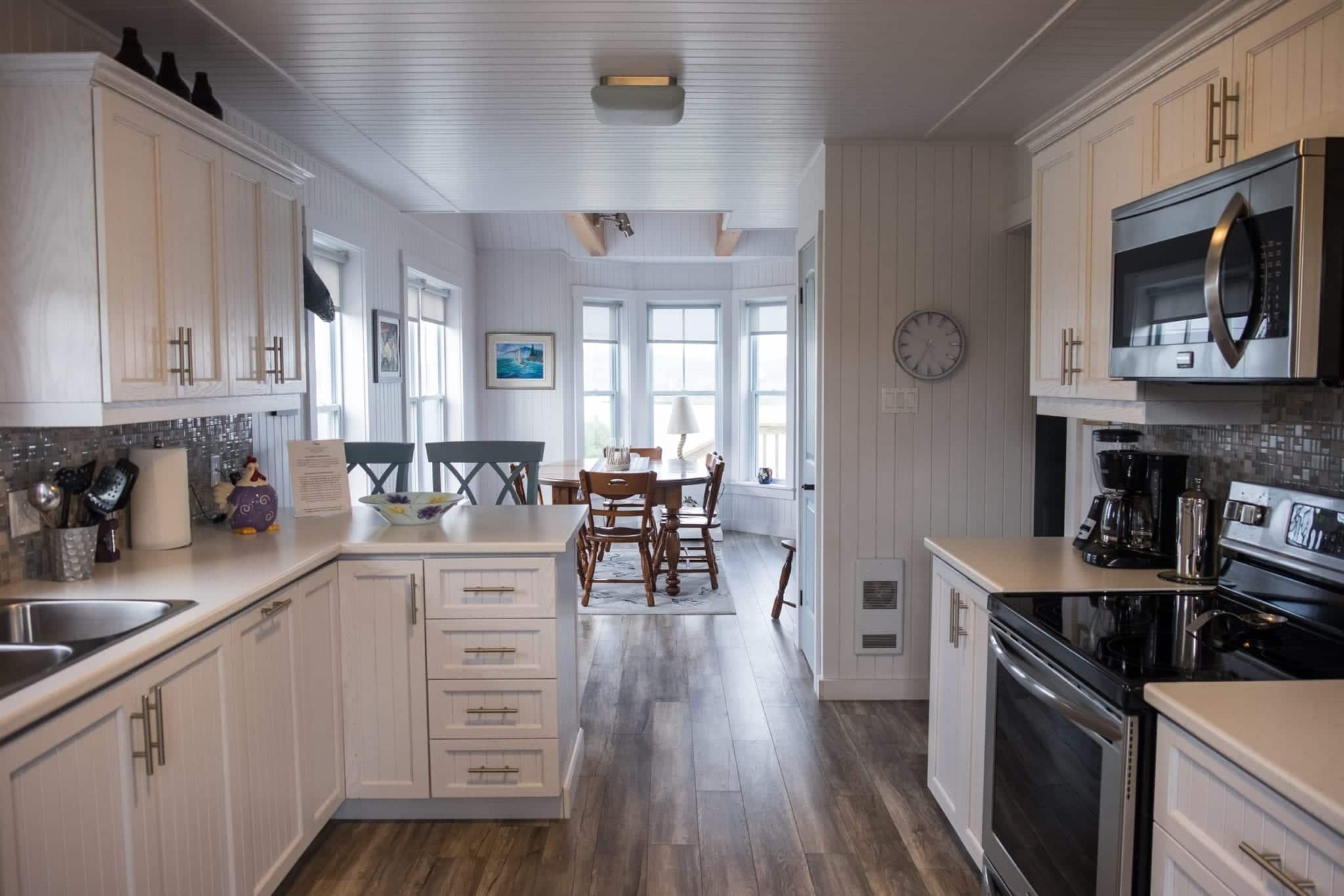 A bright white, modern kitchen leading backward into a sitting room.