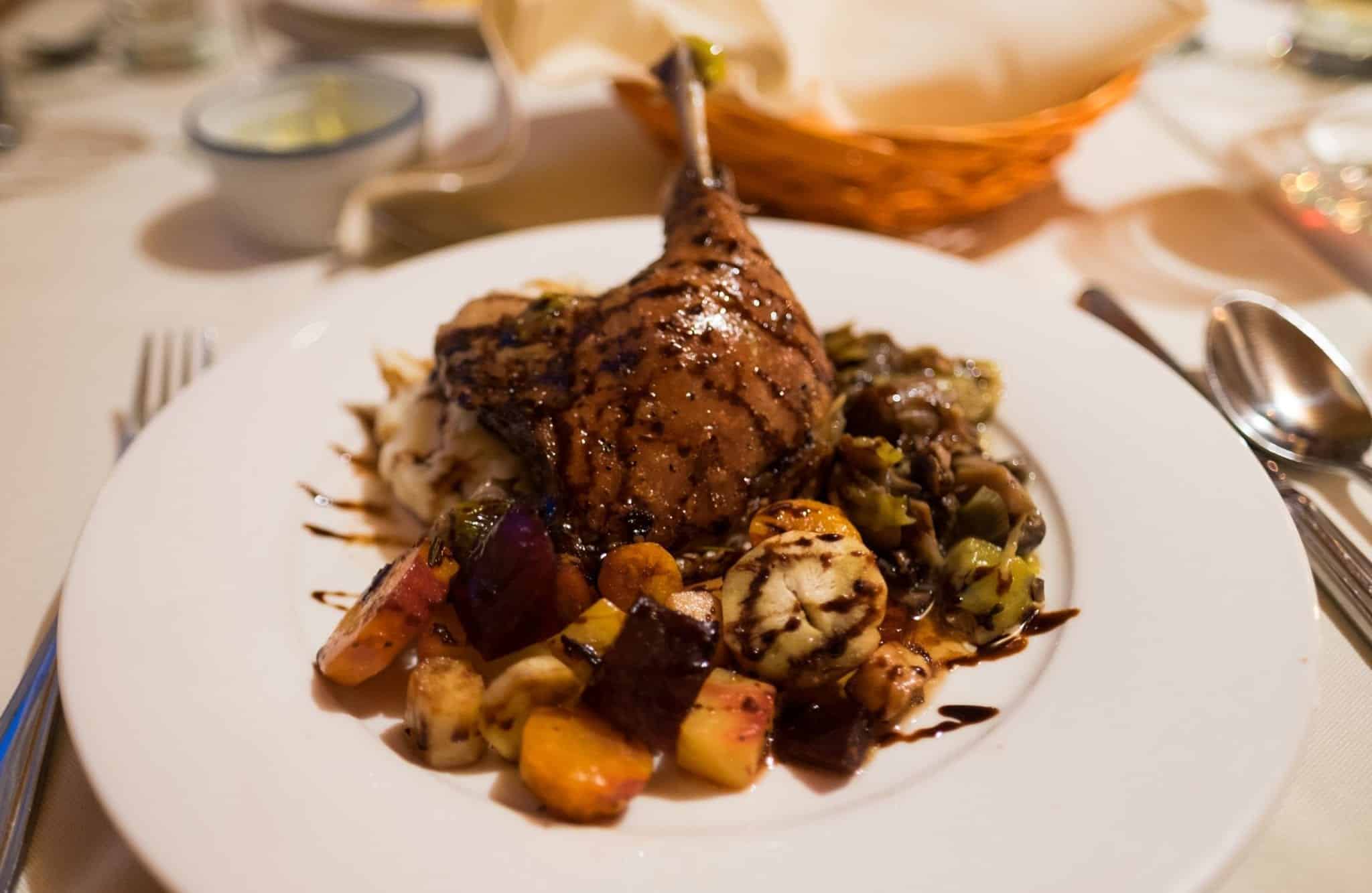 A roasted duck breast on a plate of roasted vegetables.