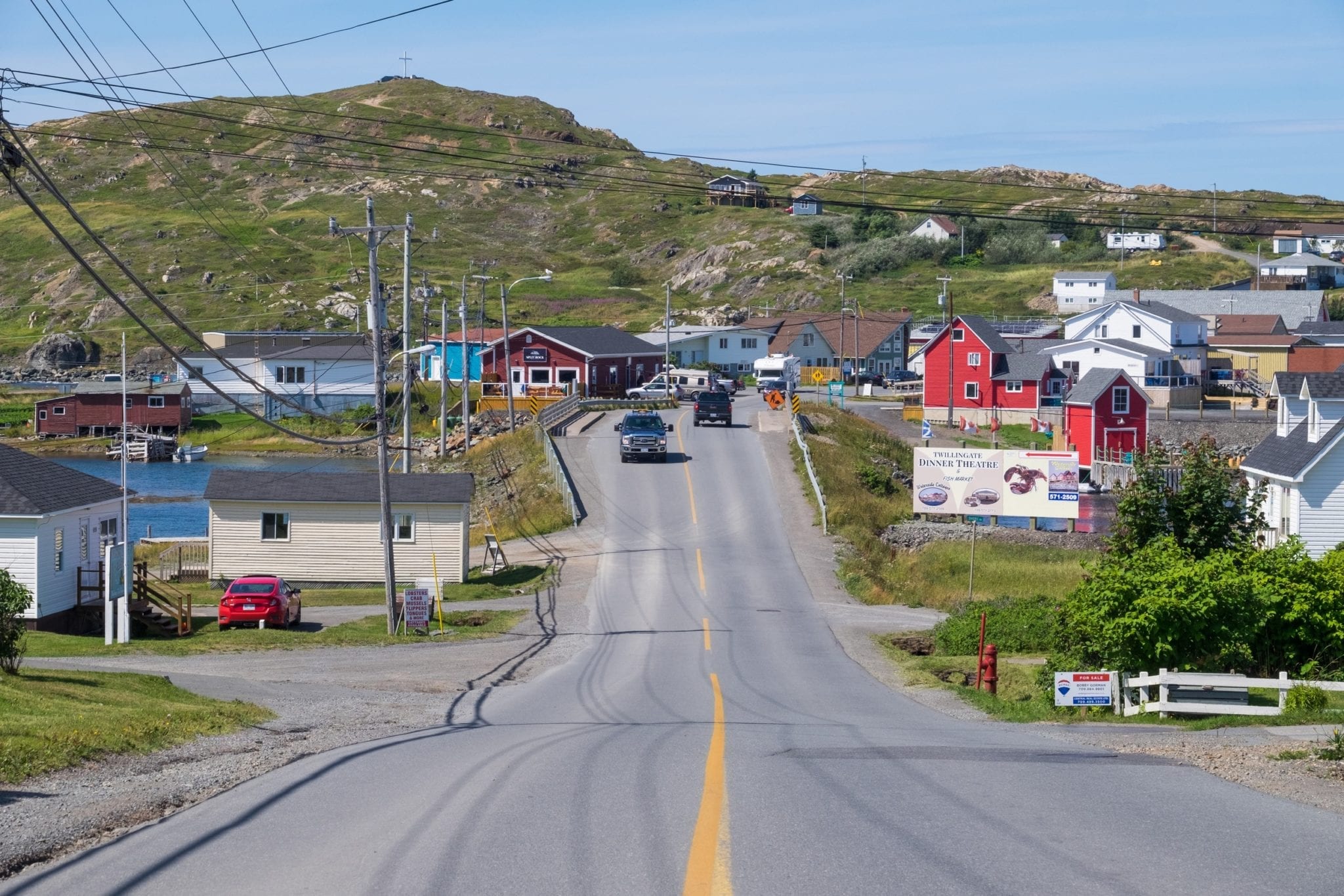 A road dips down and leads to a hilly green landscape with brightly colored houses on each side.