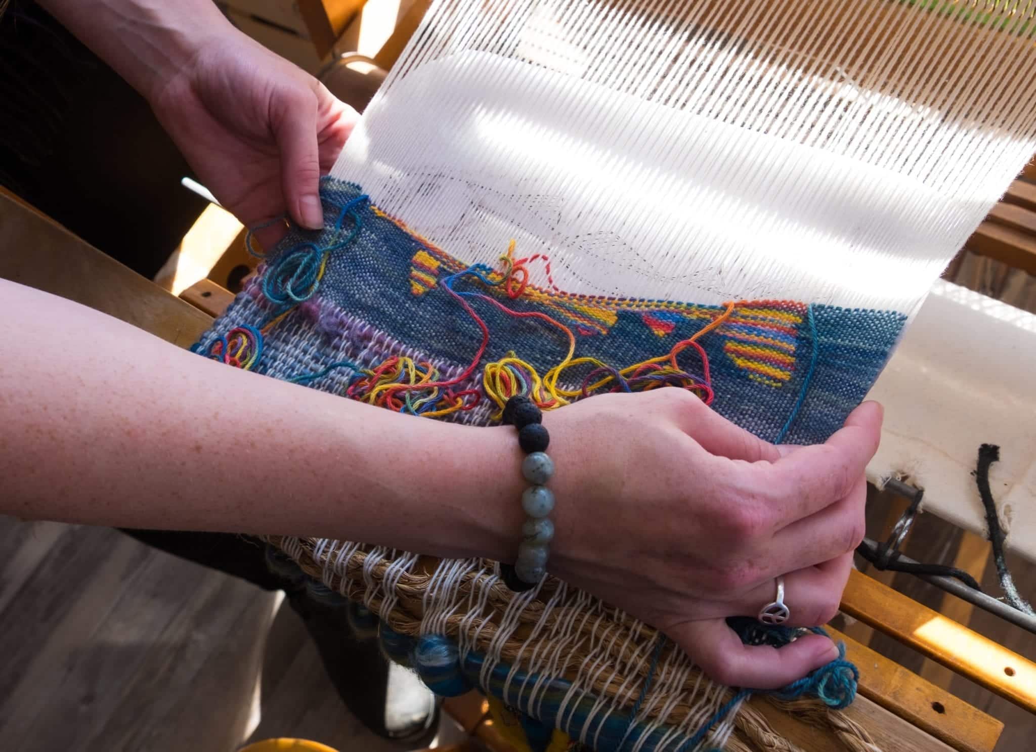 Hands holding up a partially woven fabric fish on a loom in Twillingate.